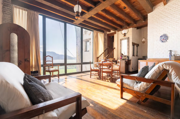 Habitación rústica luminosa con vigas de madera, grandes ventanales y vistas a la montaña.
