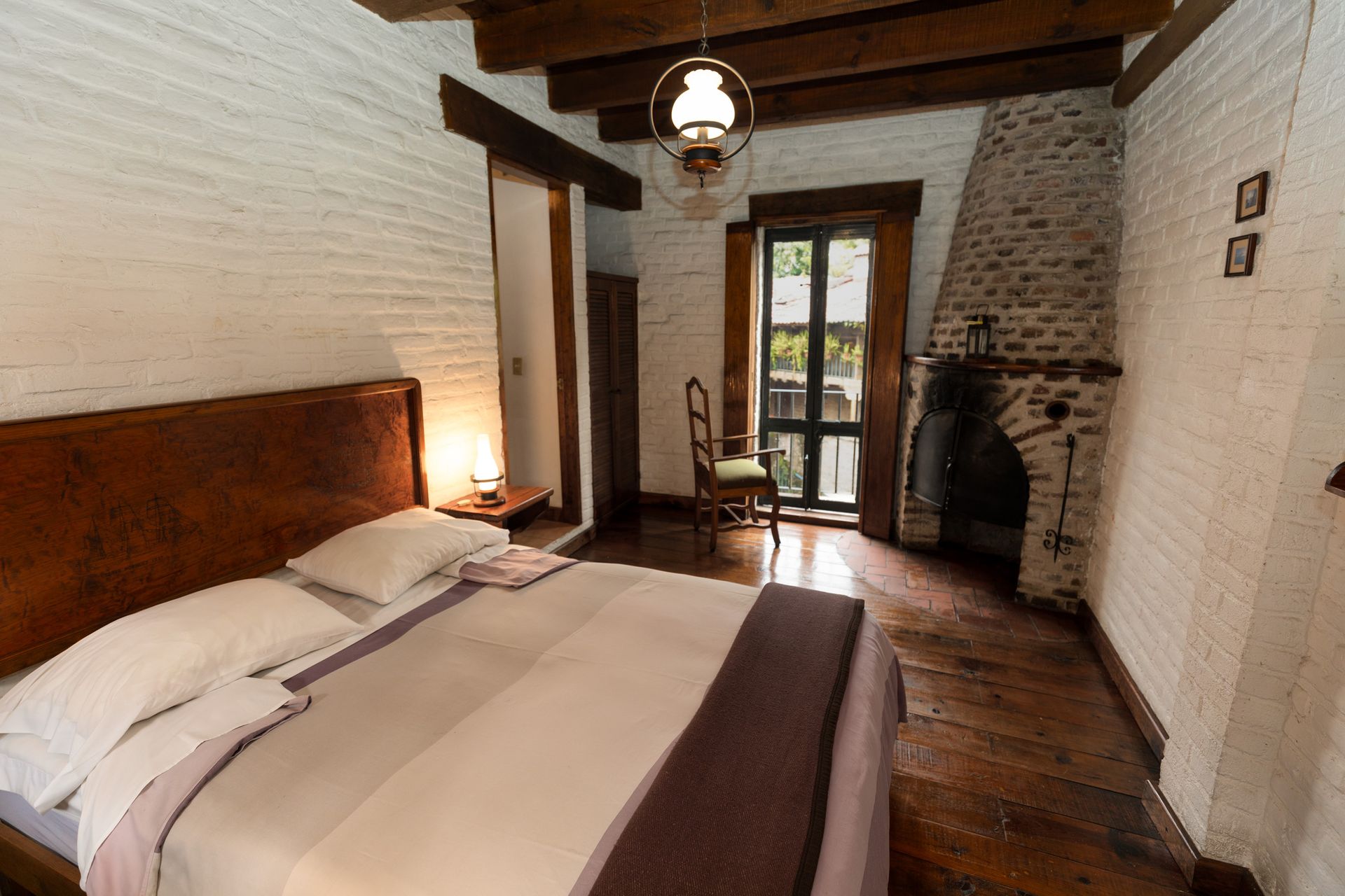 Acogedora habitación rústica con una cama grande, vigas de madera, chimenea de piedra y puertas francesas.