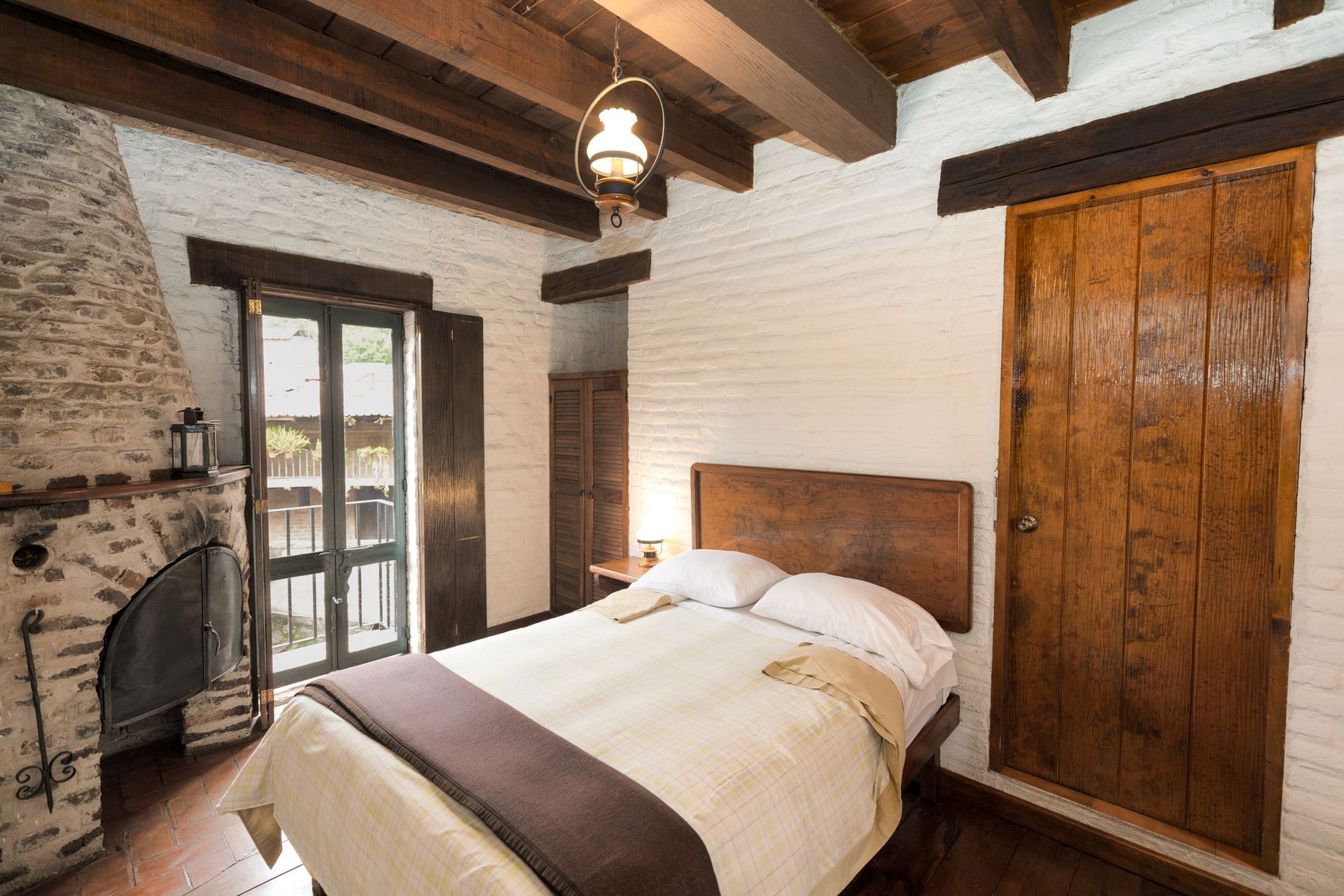 Dormitorio rústico con vigas de madera a la vista, paredes de ladrillo blanco, una cama, chimenea y puertas de armario.