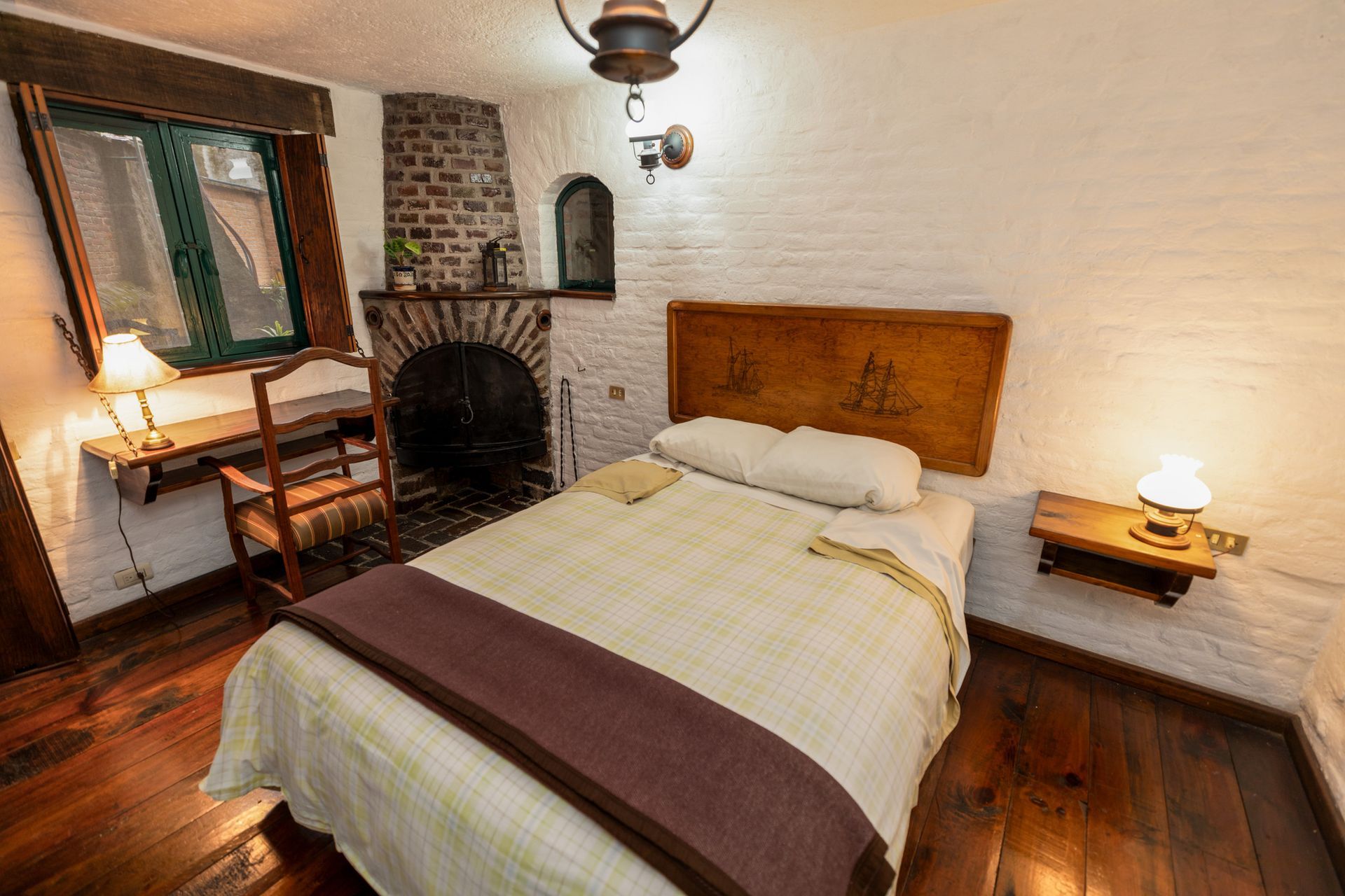 Habitación acogedora con cama, chimenea de ladrillo, muebles de madera e iluminación ambiental cálida.