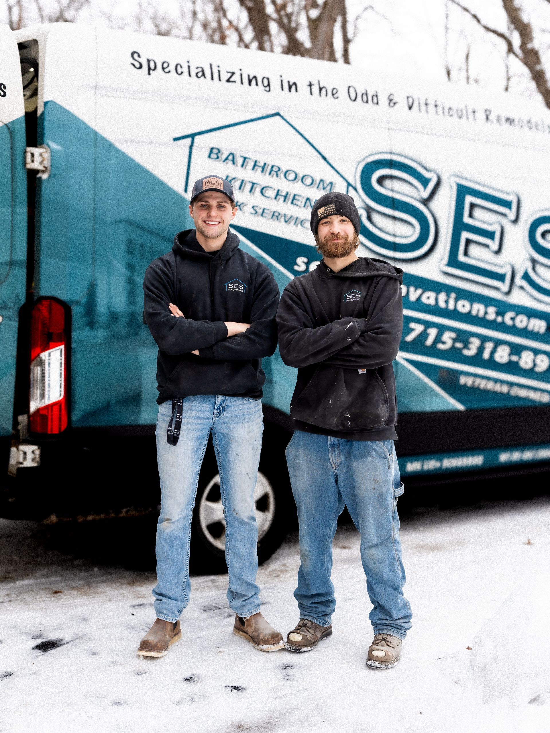 Two men standing in front of a blue and white service truck, arms crossed, on a snowy street