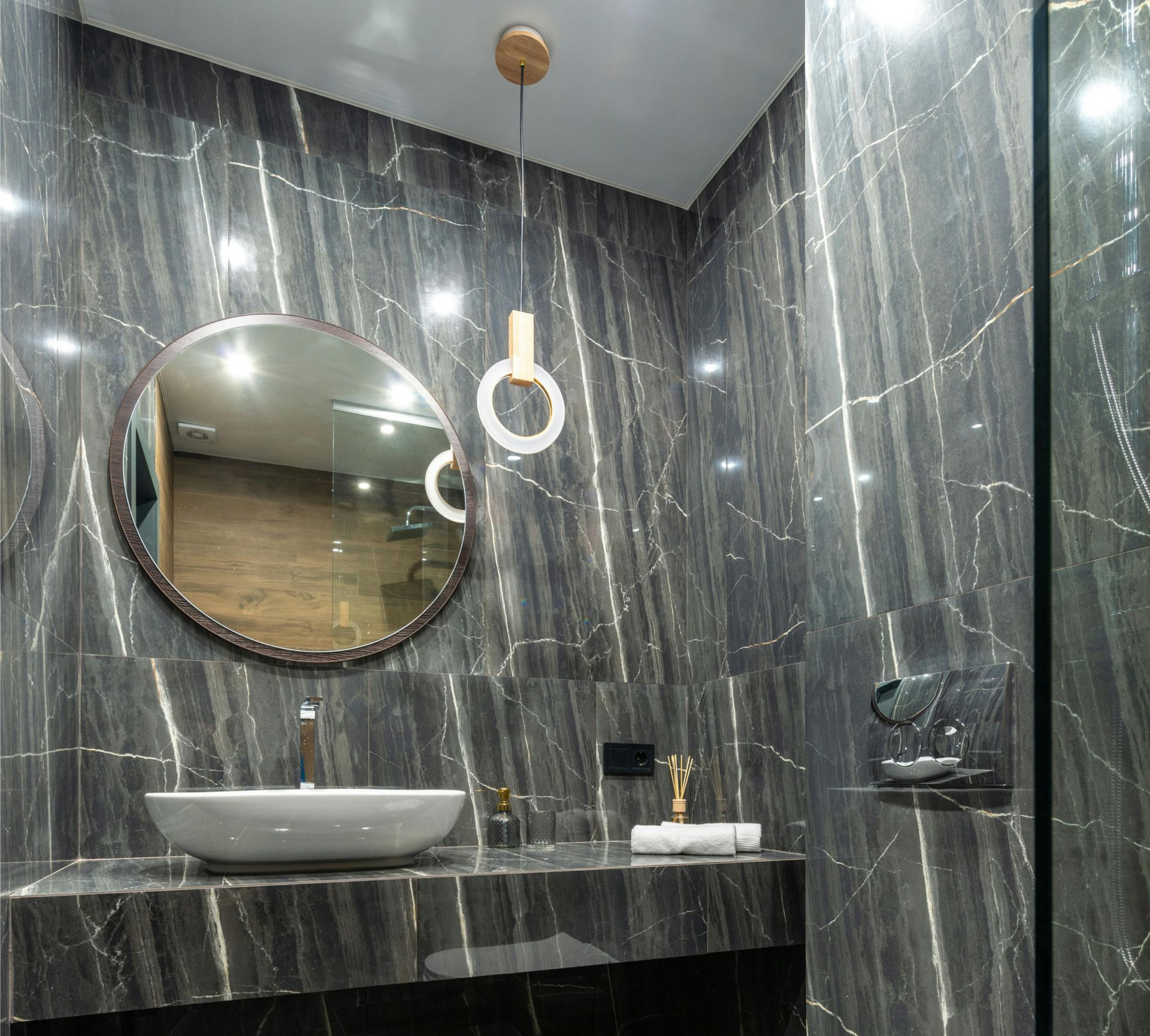 Modern bathroom with dark gray marble walls, round mirror, and vessel sink.