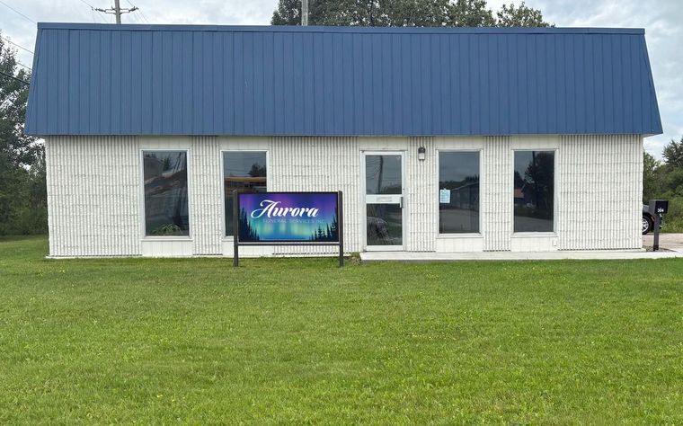 Small white building with blue roof and a colorful sign, set on a grassy lawn.