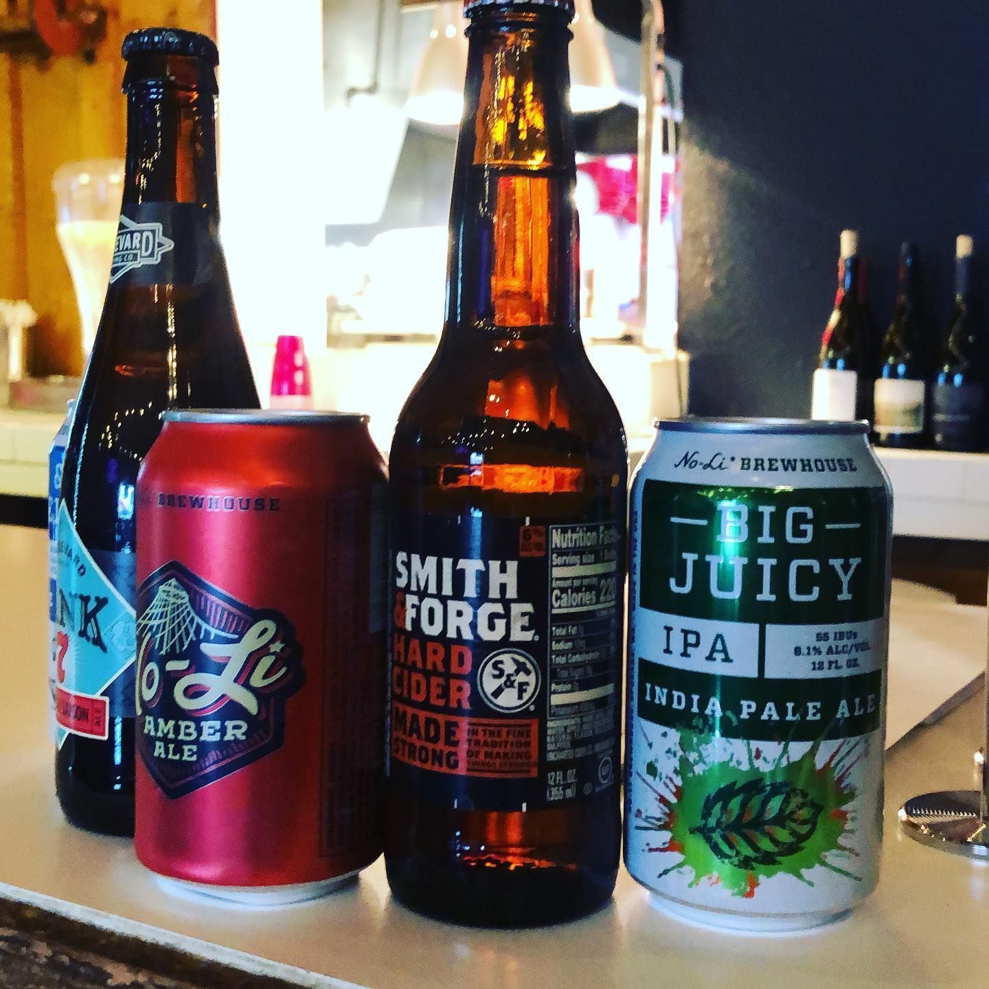 A bottle of smith forge brand cider sits next to a can of big juicy ipa