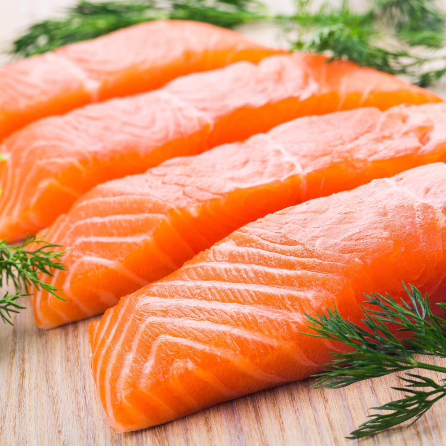 Three pieces of salmon are sitting on a wooden table.