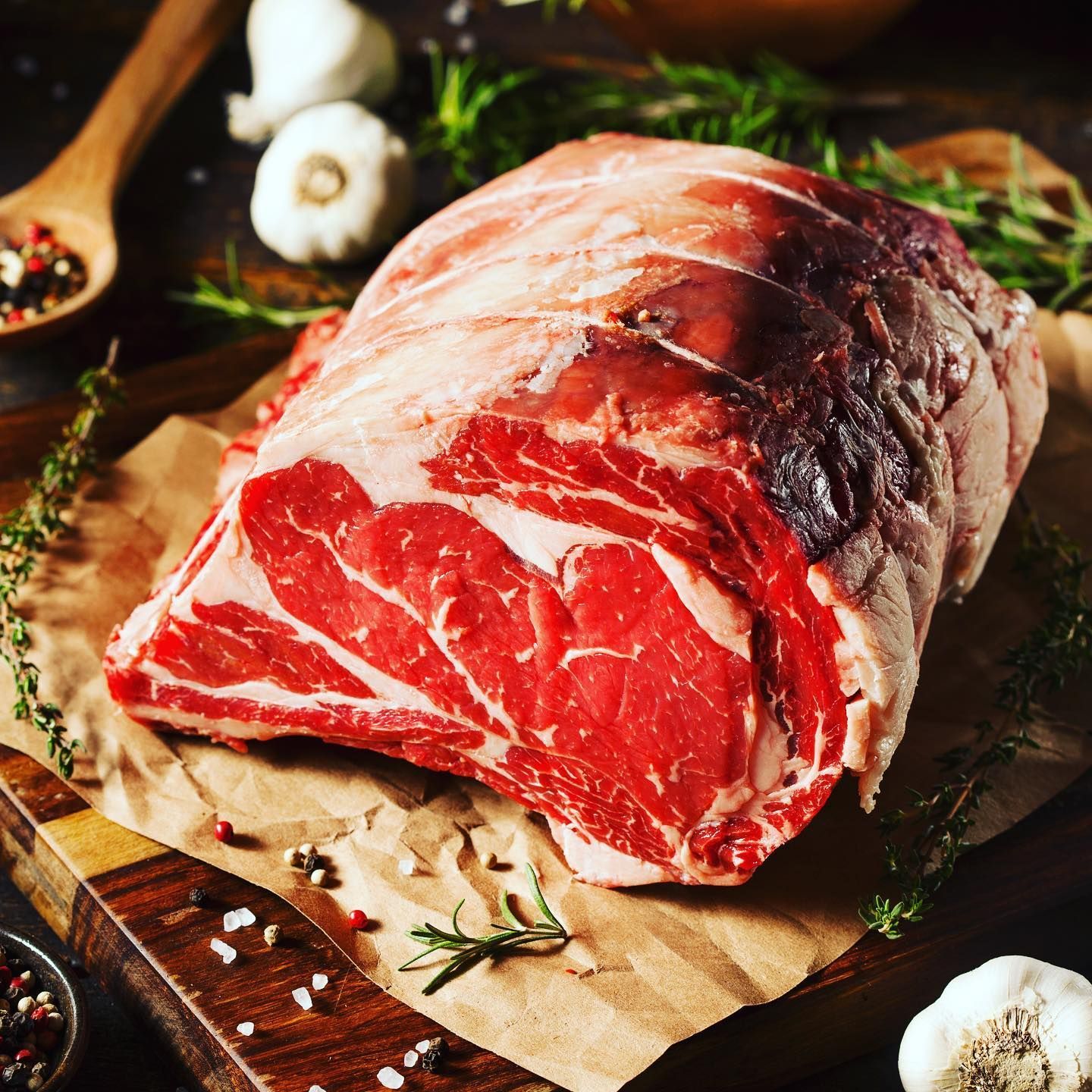 A large piece of raw beef is sitting on a wooden cutting board.