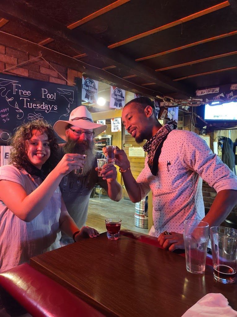 A group of people are standing at a bar toasting with shot glasses.