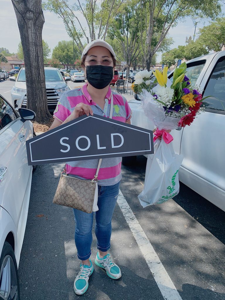 Person holding a “SOLD” sign in a parking lot beside a decorated car.