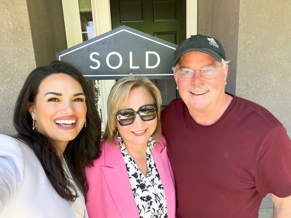 Three smiling people pose in front of a sold real estate sign.
