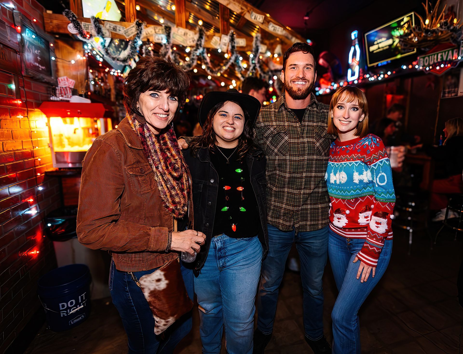 Four people posing together in a warmly lit bar decorated with string lights and colorful holiday decor.
