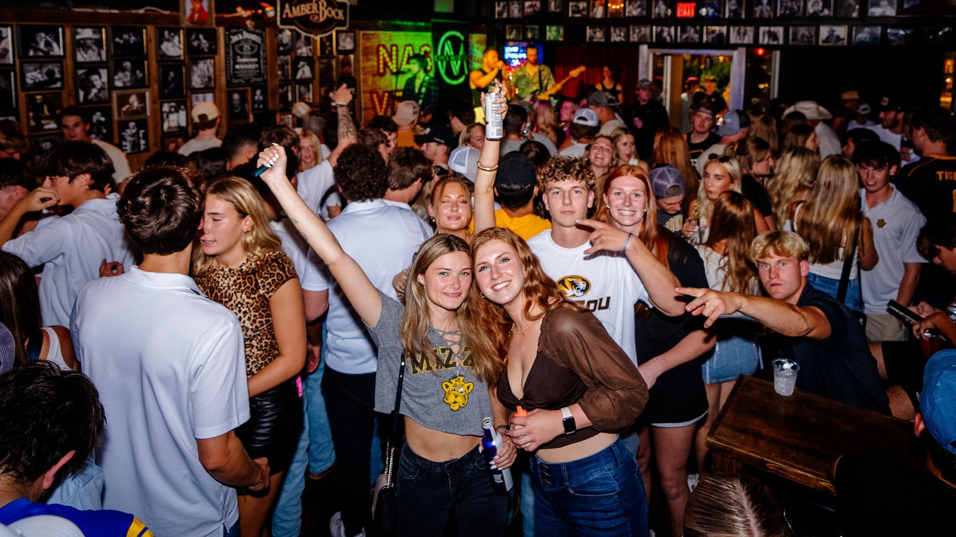 Crowded nightclub dance floor with people raising their hands and smiling under colorful lights