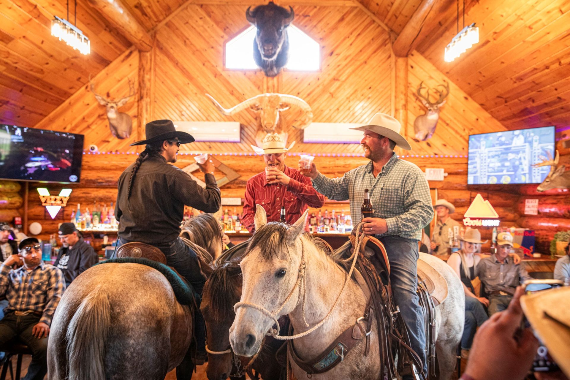 Cowboys on horses inside a rustic lodge, gathered around a raised performer under warm lights.