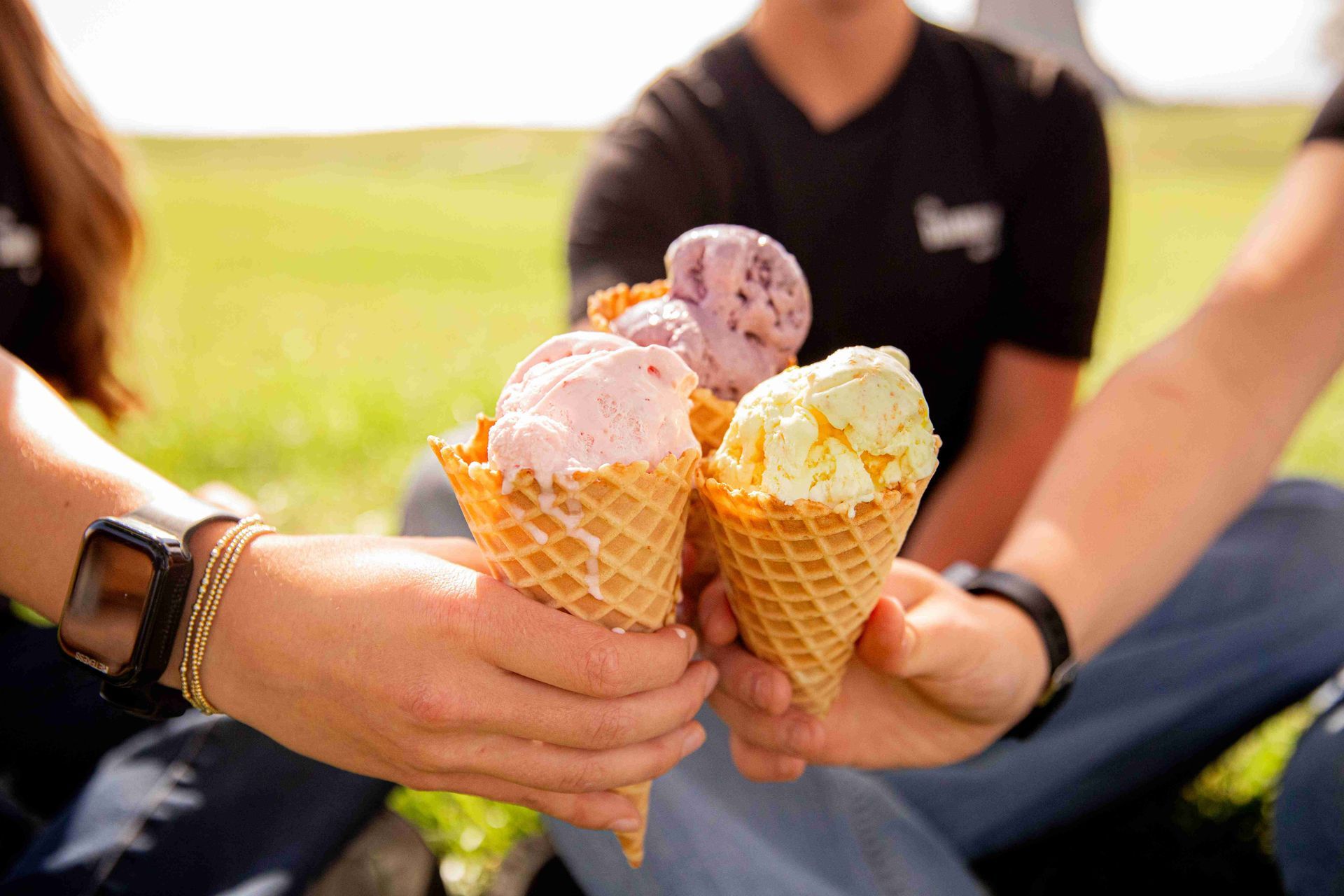 Three people holding waffle cones with ice cream outdoors on a sunny day