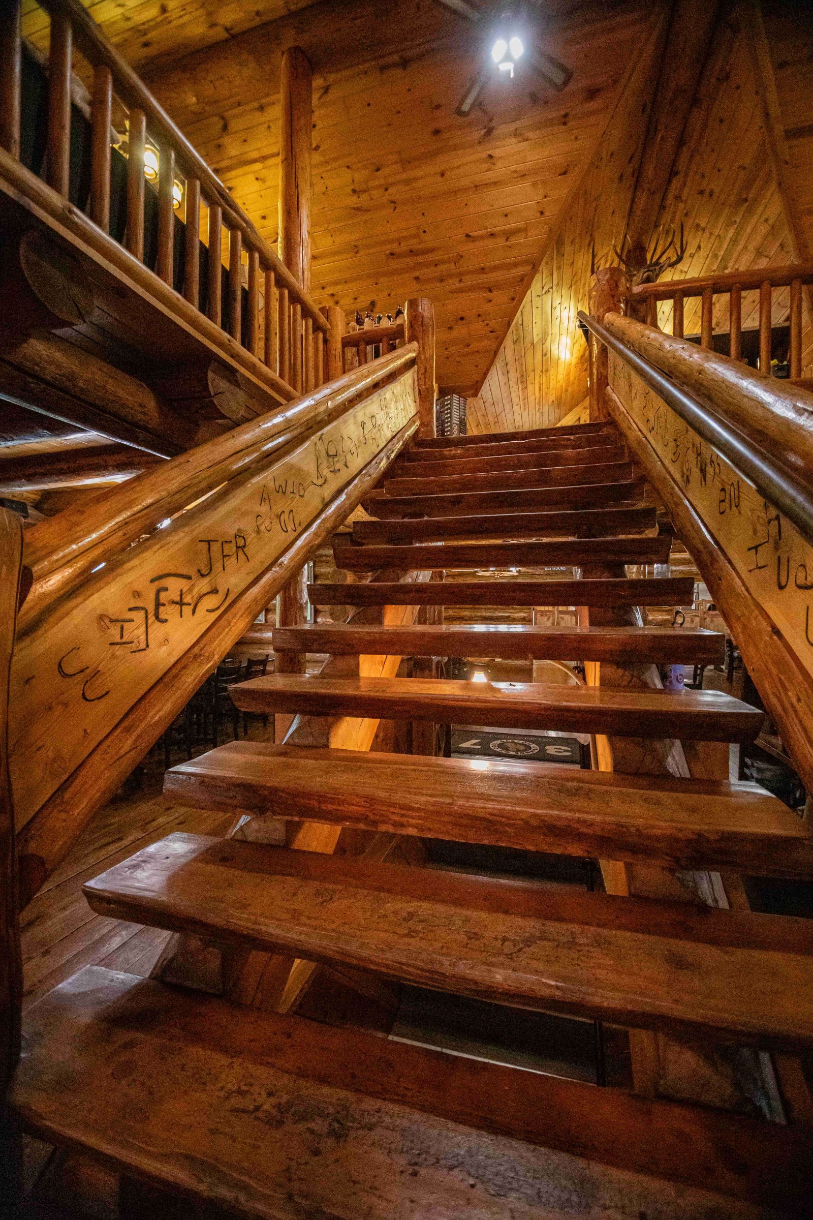 Wooden staircase in a warm, rustic interior, lit from above with railings on both sides.