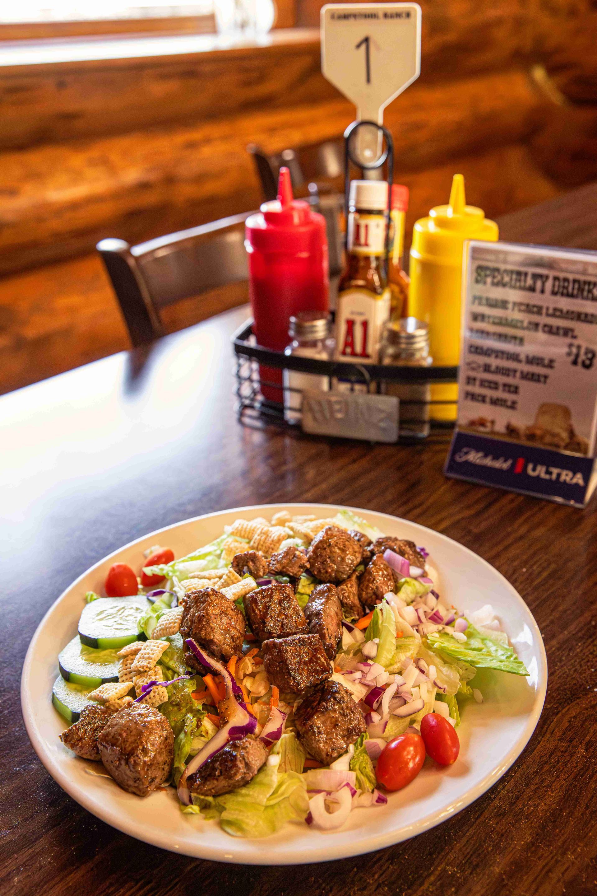 Plate of salad with grilled chicken on a wooden table beside condiments and a table number sign