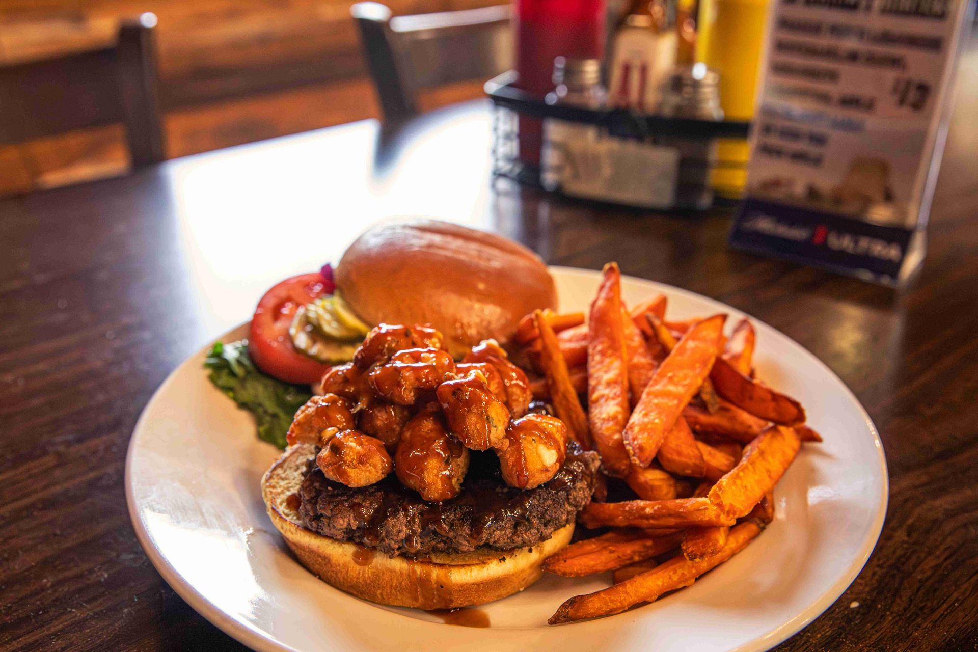Burger topped with sauce and fries on a white plate in a restaurant