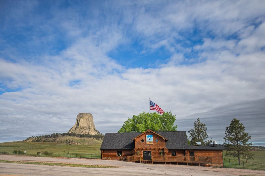 Rustic lodge with U.S. flag near a rock butte under a cloudy blue sky