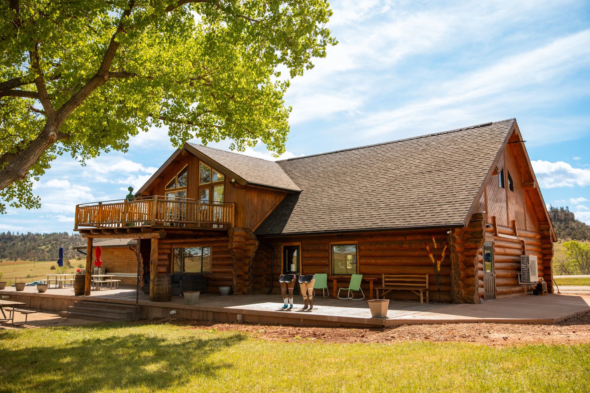 Rustic log cabin with porch under a leafy tree in a sunny rural setting