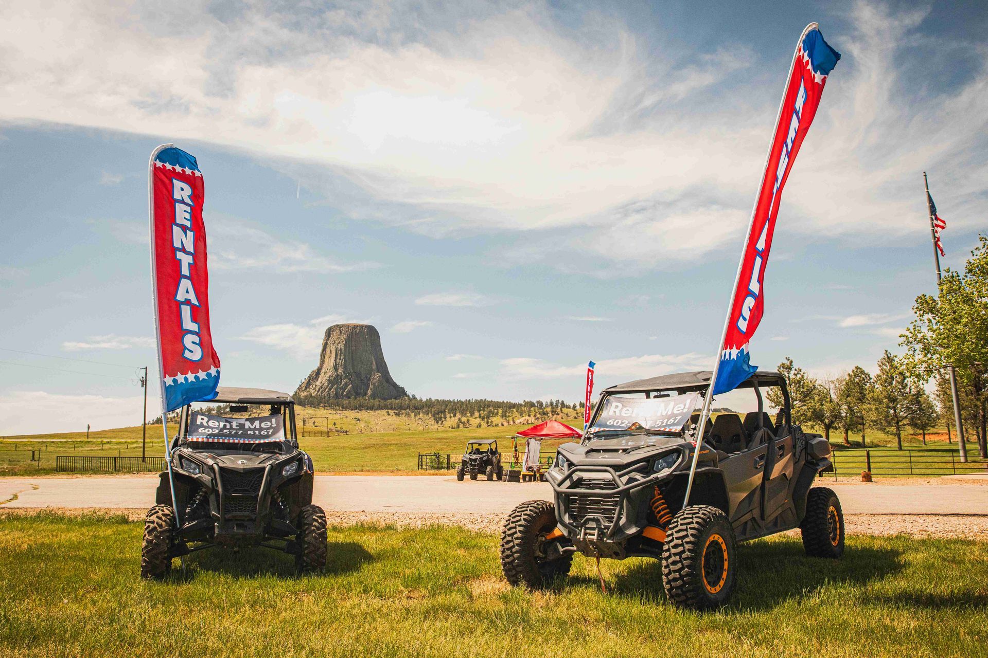 Two off-road buggies with red flags on a grassy field near a rock outcrop under a cloudy sky