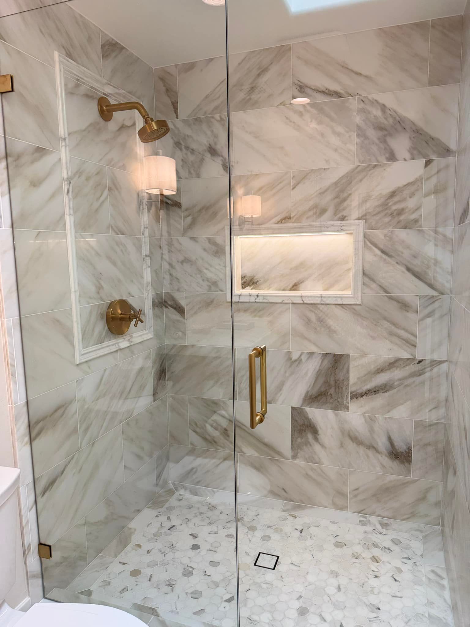 A bathroom with marble tiles and a walk in shower with a glass door.