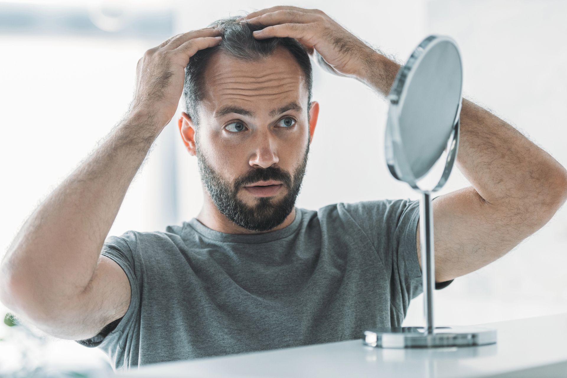 Un uomo si guarda allo specchio, esamina l'attaccatura dei capelli con le mani, con espressione preoccupata.