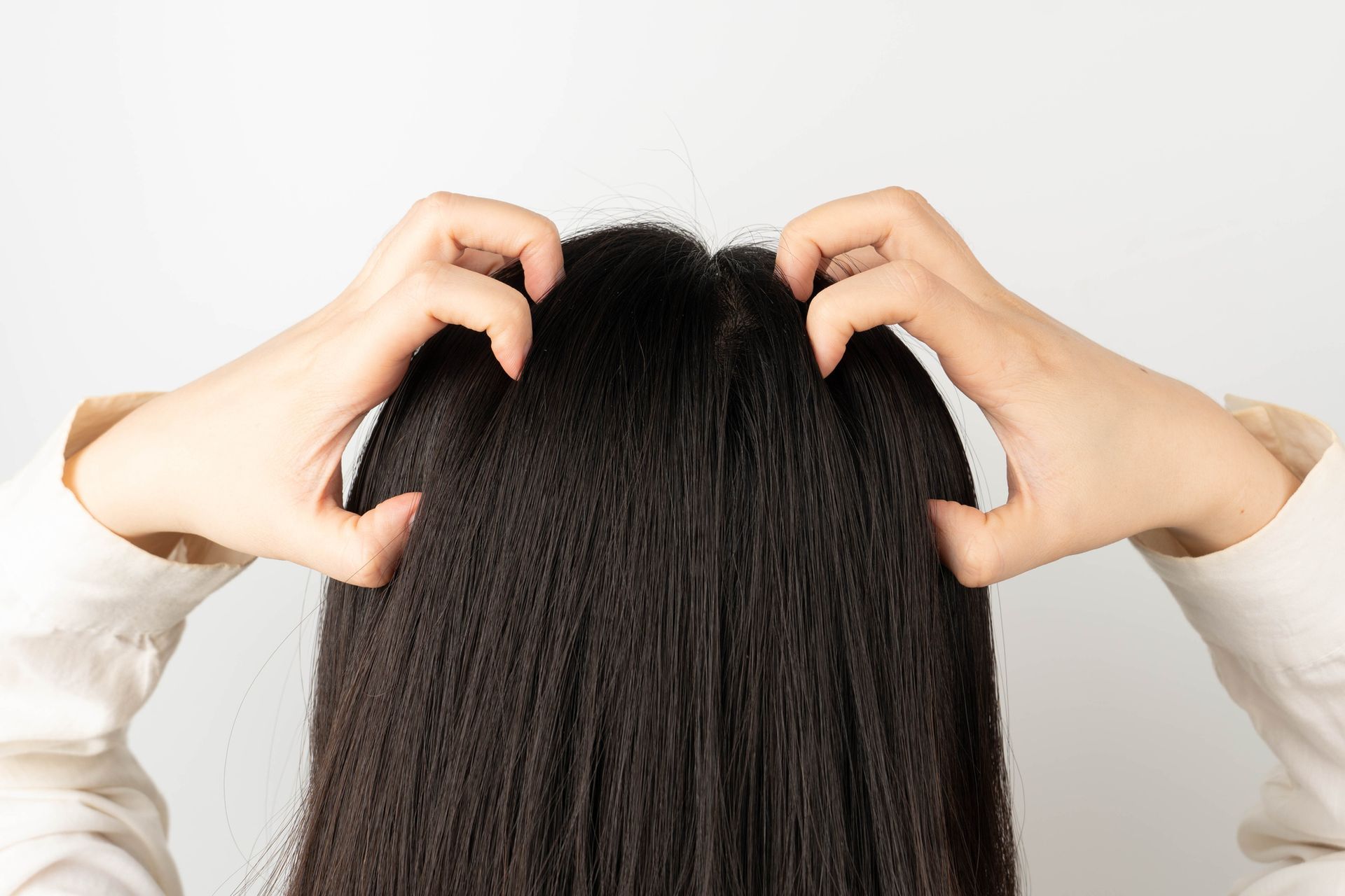 Persona che si gratta la testa, primo piano di capelli scuri, su sfondo bianco.