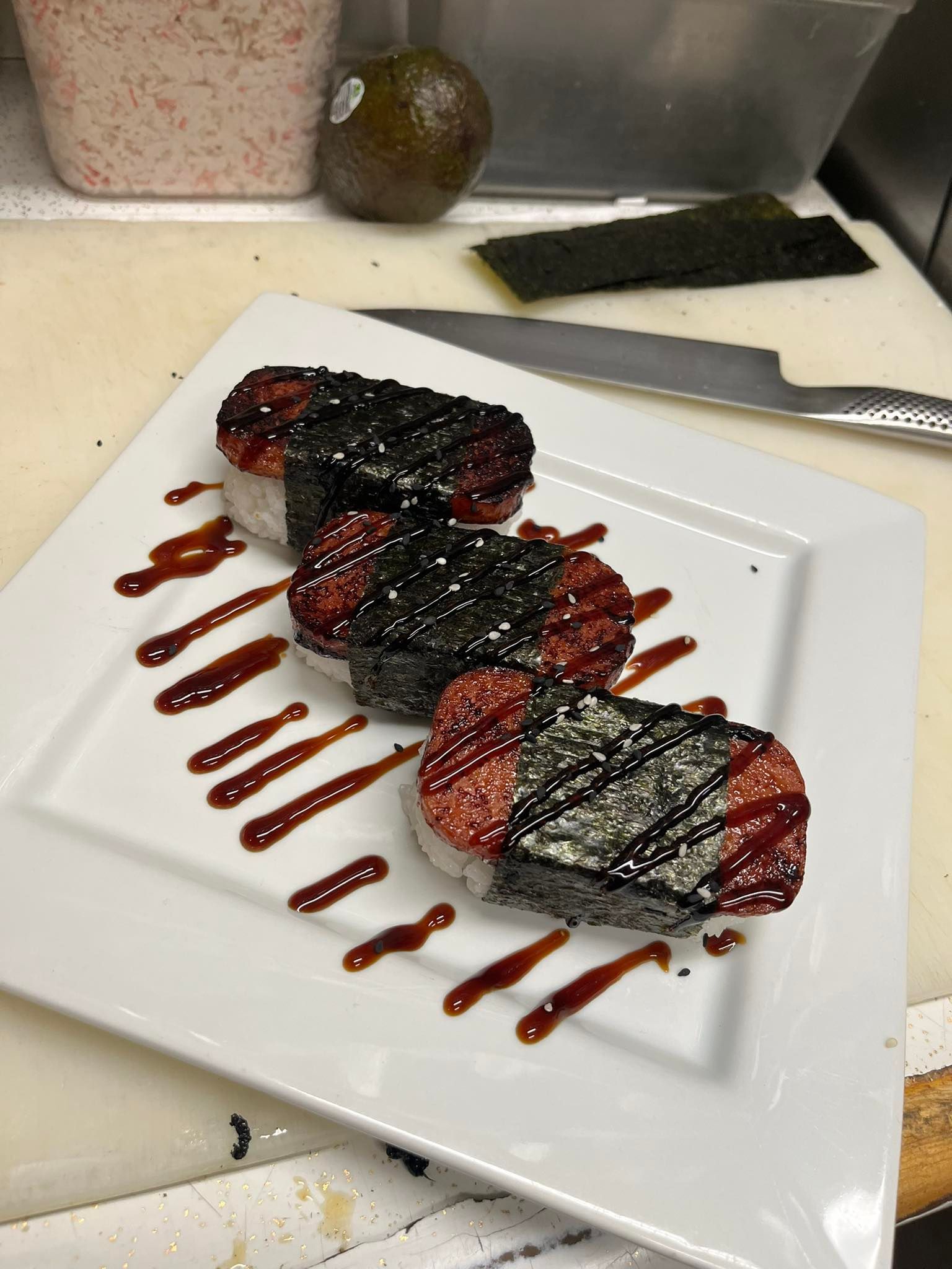 Three berry-topped rolled desserts drizzled with chocolate on a white plate by a kitchen knife