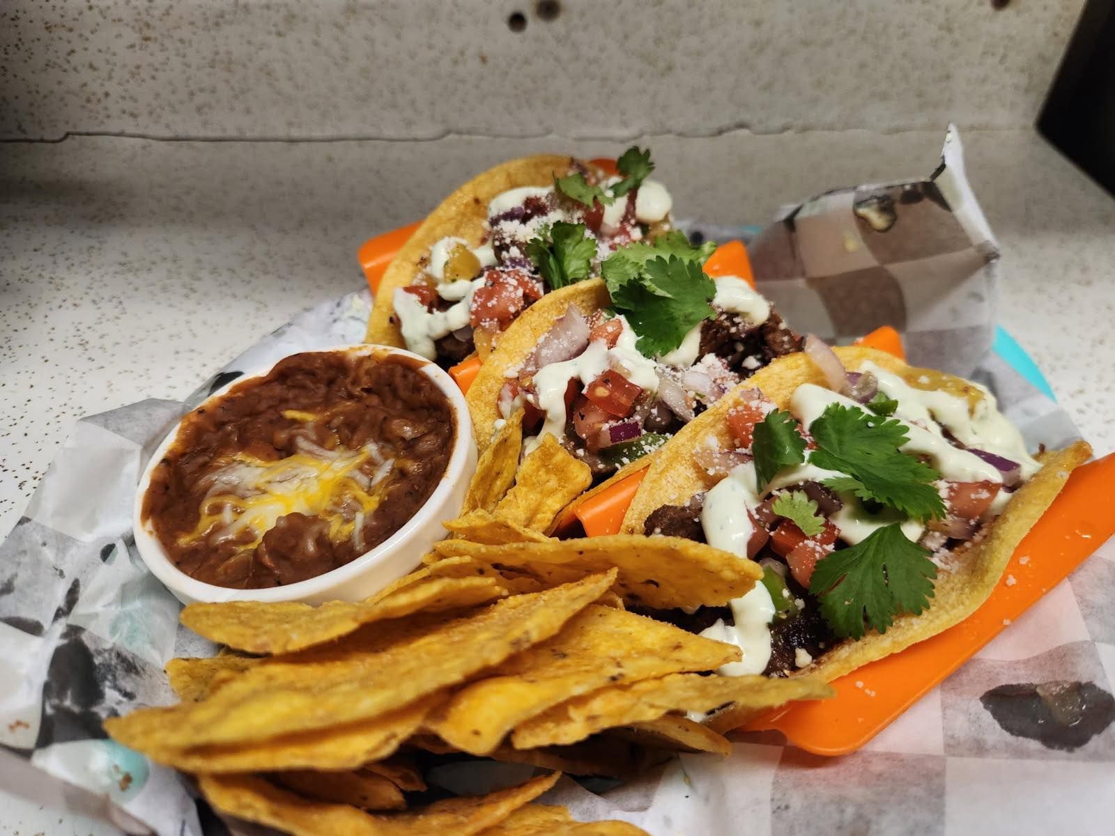 Tacos with cilantro and white sauce beside a bowl of beans and tortilla chips on a counter