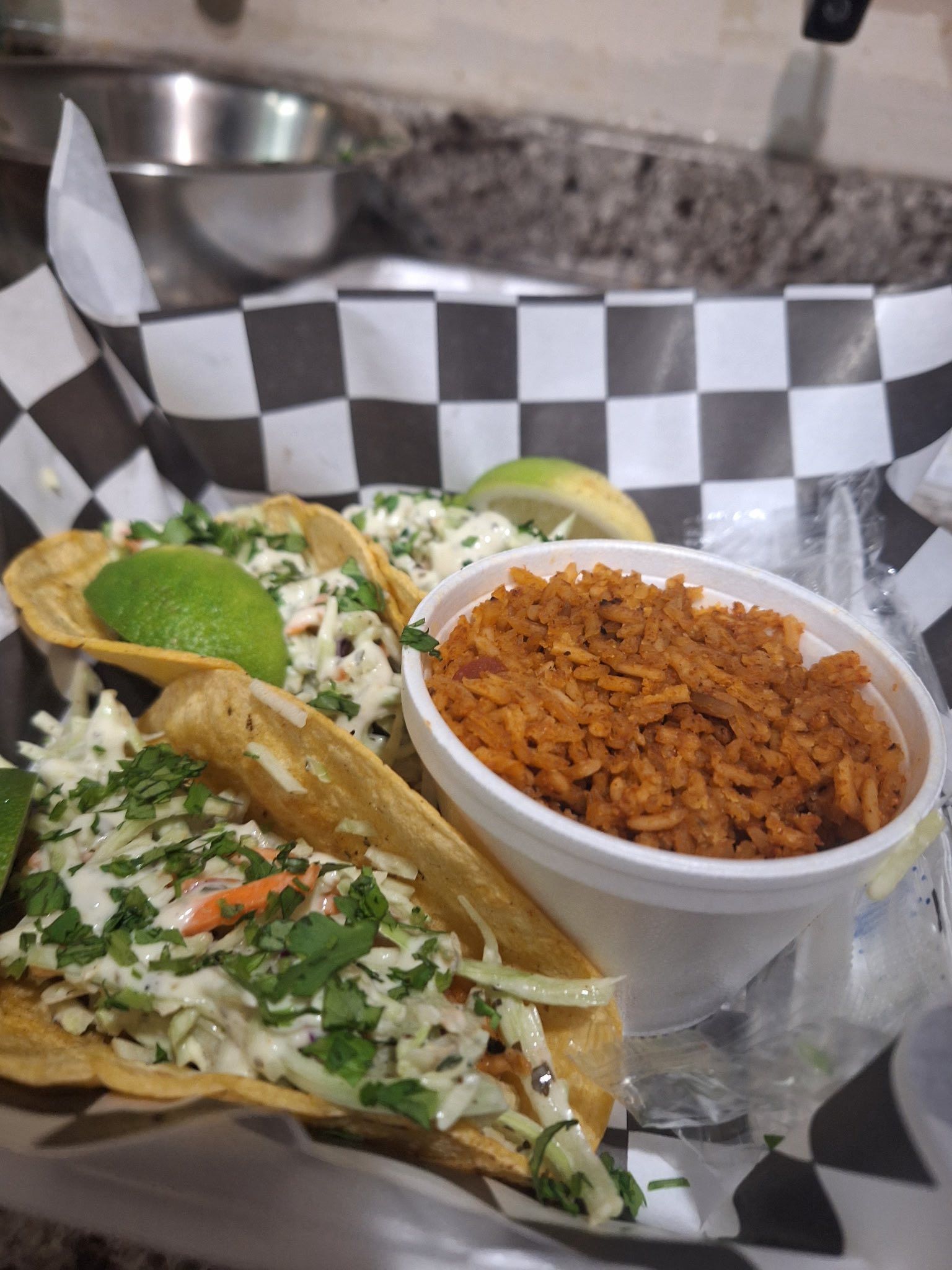 Three tacos topped with cilantro and lime beside a bowl of red rice on a tray.