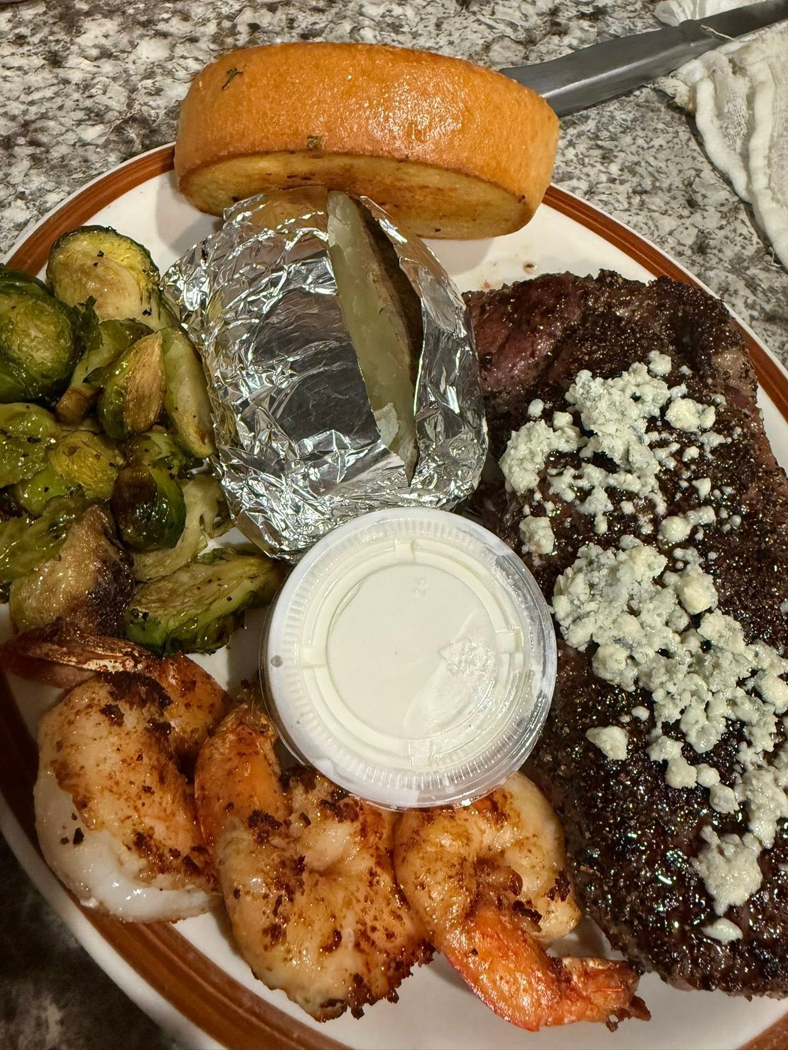 Plate with a sandwich, grilled chicken, zucchini, a foil-wrapped item, dip, and beans topped with crumbled cheese