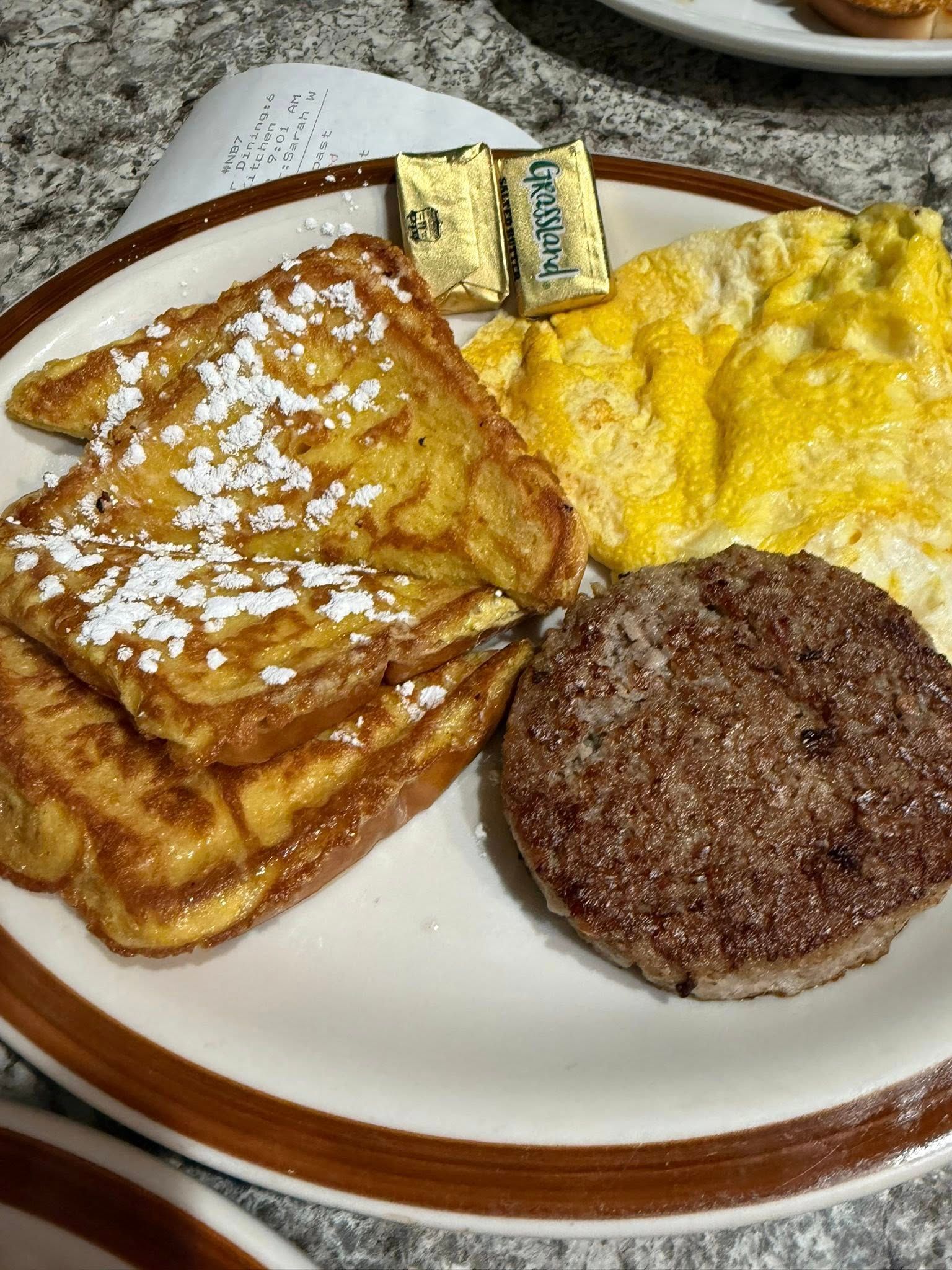 Plate of breakfast food: French toast, scrambled eggs, sausage patty, and butter on a white plate.