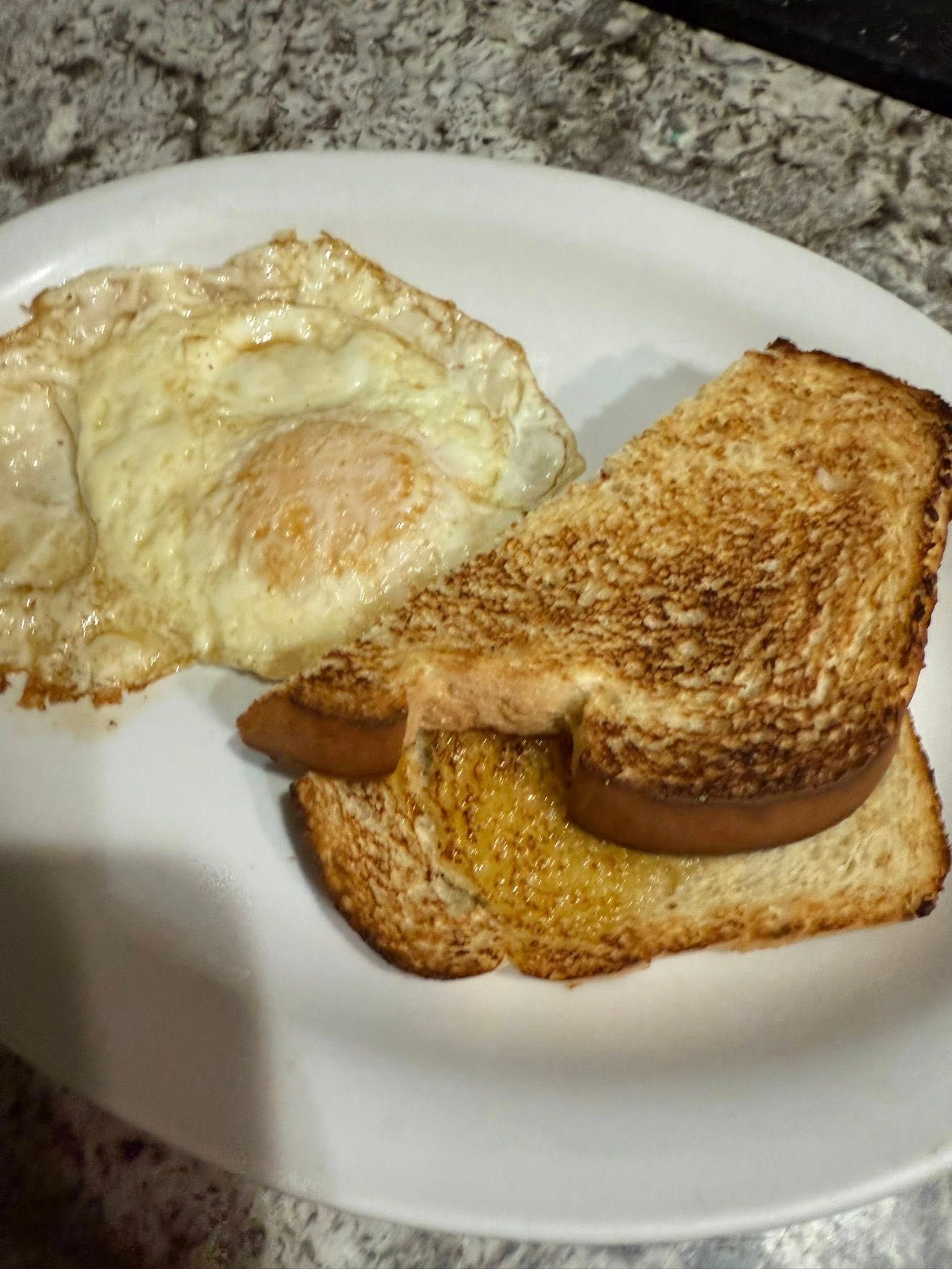 Fried egg and toasted sandwich on a white plate on a granite countertop
