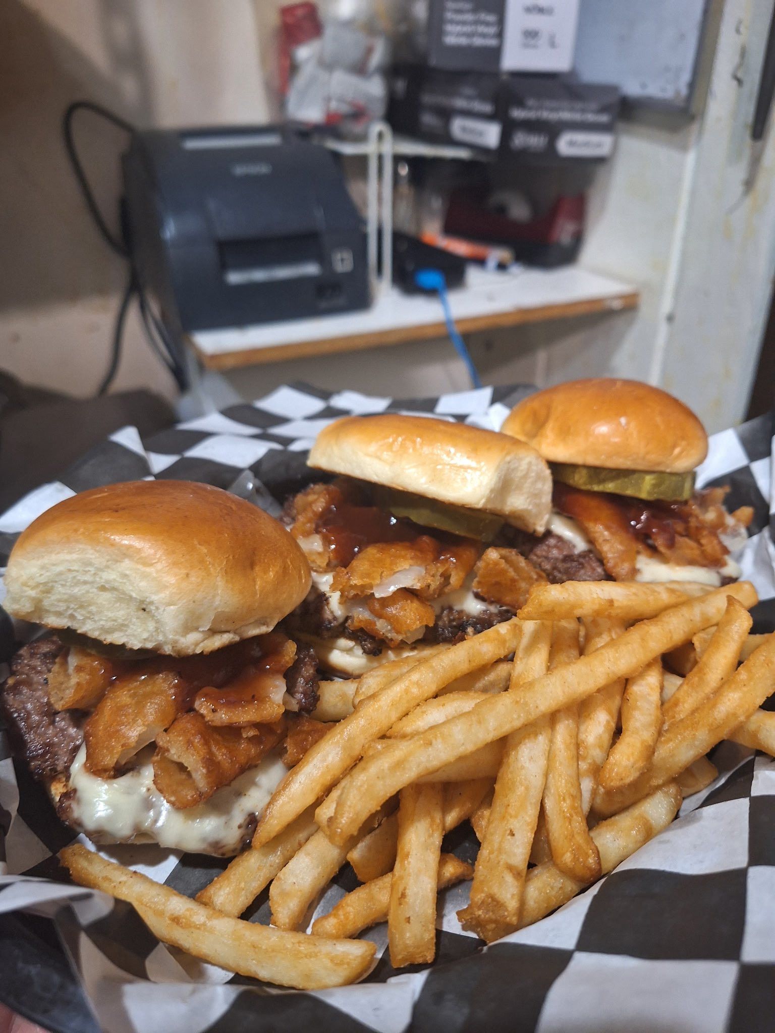 Three barbecue chicken sliders with fries on checkered paper in a restaurant setting