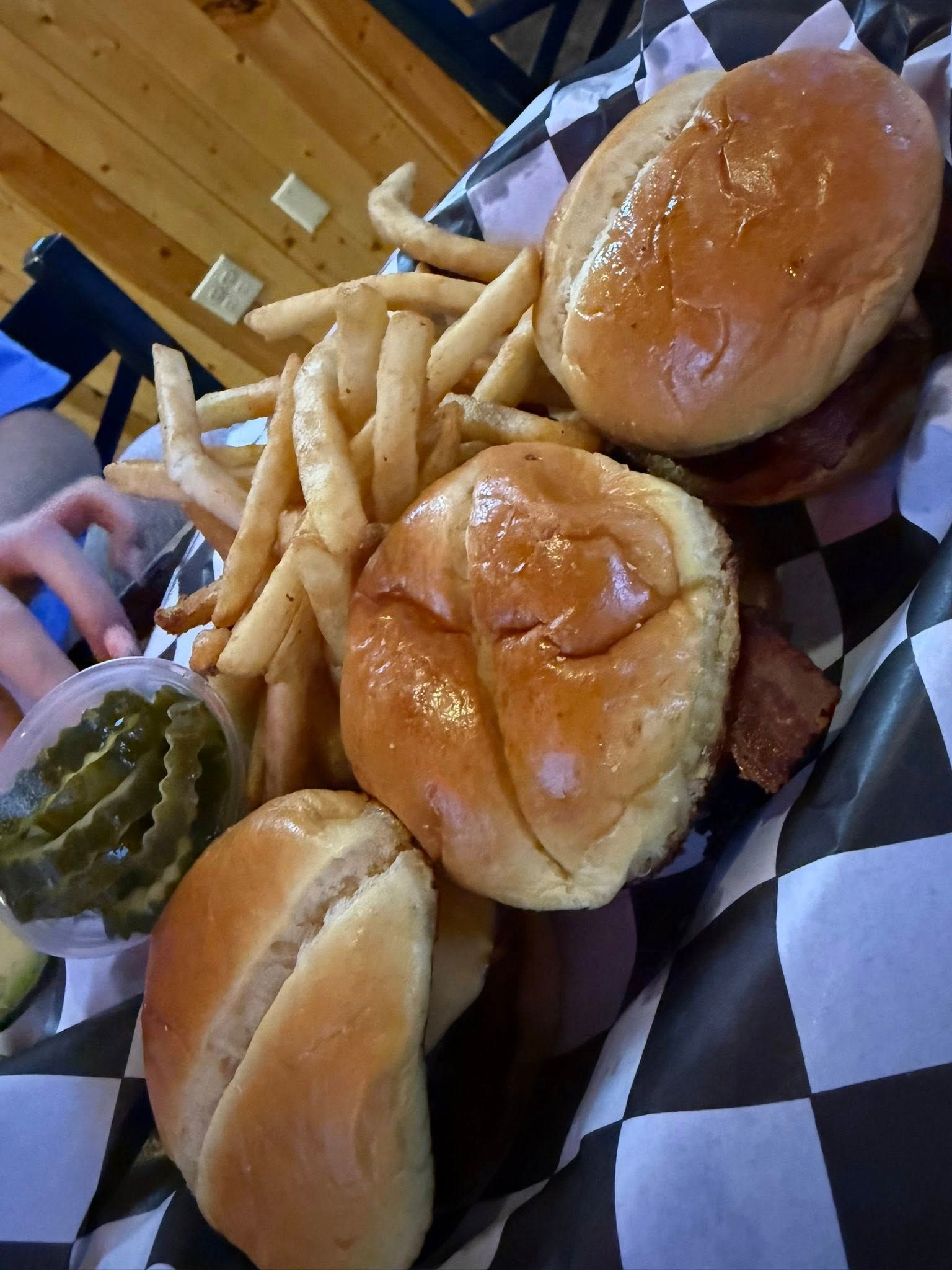 Burger meal with fries and pickles on black-and-white checkered paper in a restaurant