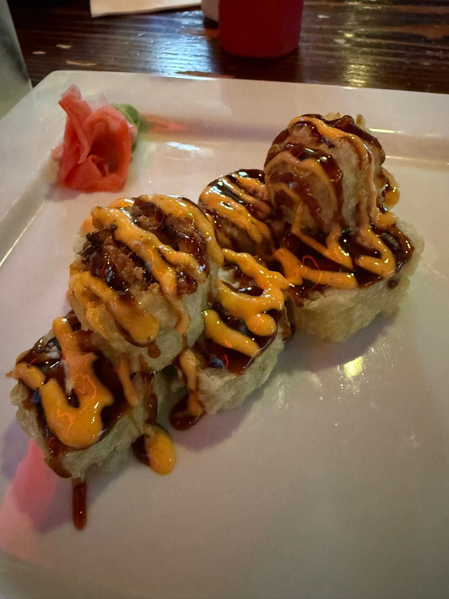 Sushi rolls topped with sauce on a white plate, with pickled ginger on the side.