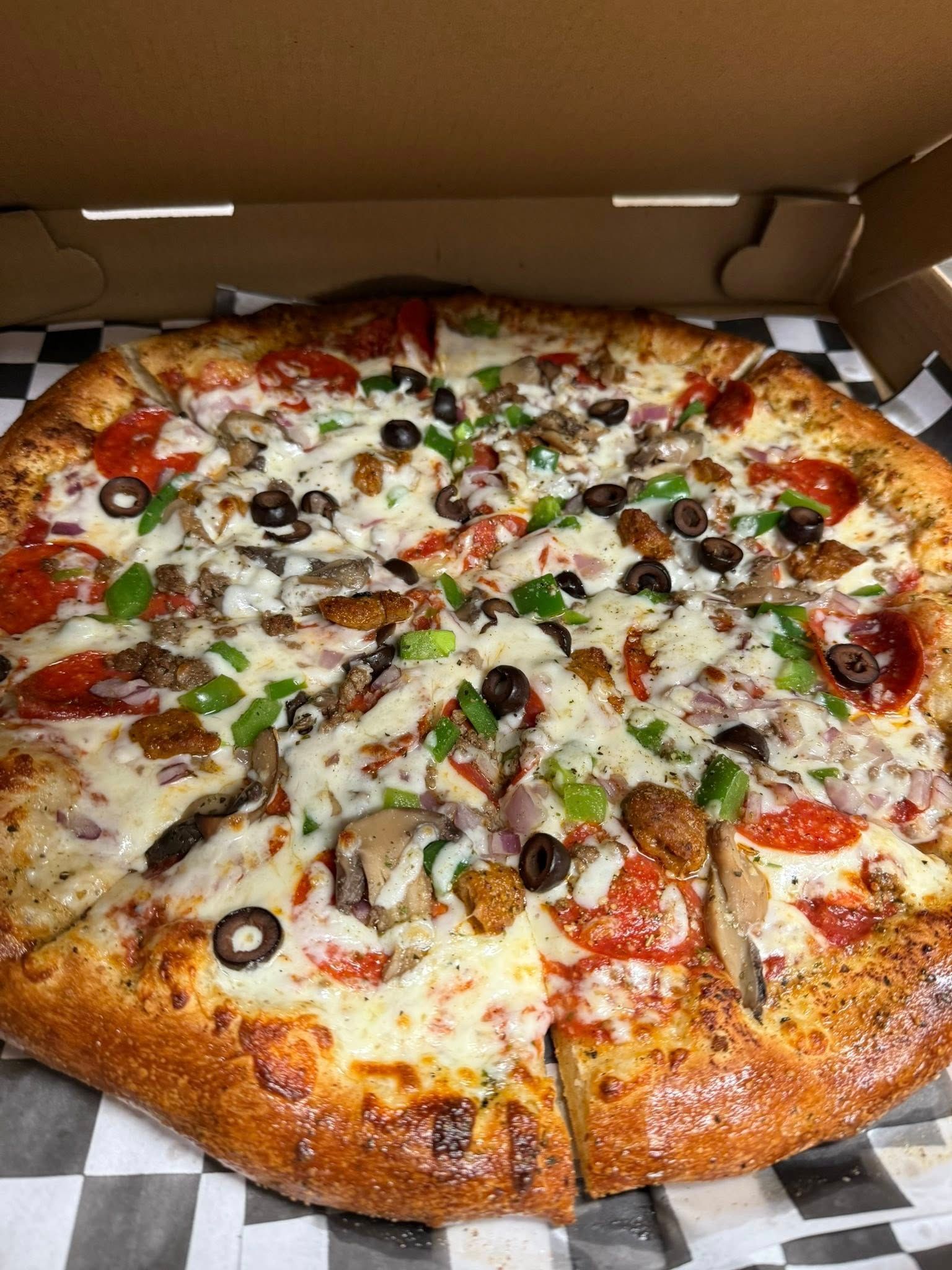 Large pepperoni and veggie pizza in a cardboard box, sliced into wedges