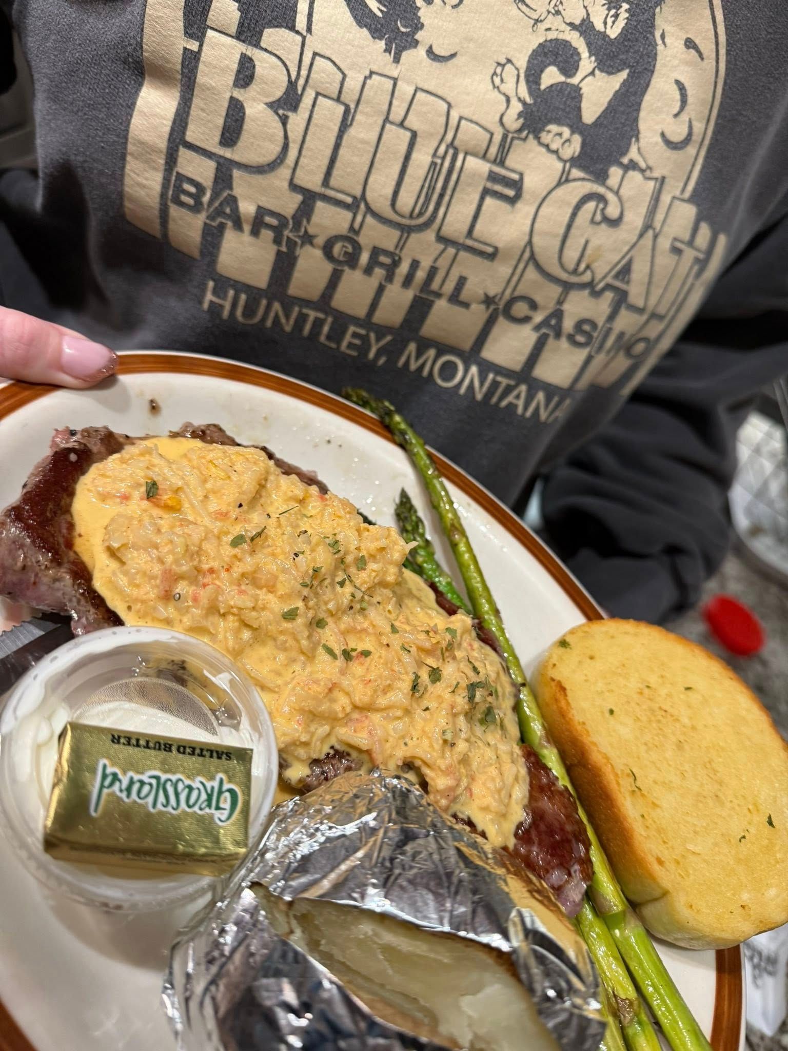 Person holding a plate with an omelet, sausage, biscuit, honey, and a drink on a table outdoors