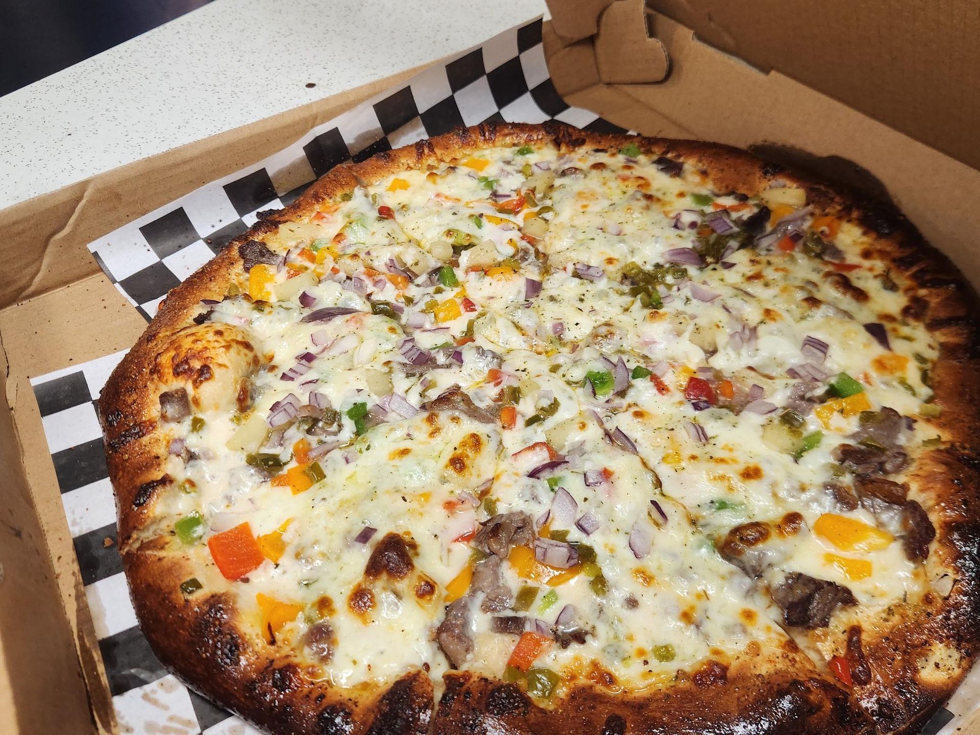 Cheesy vegetable pizza in a cardboard box with a browned crust