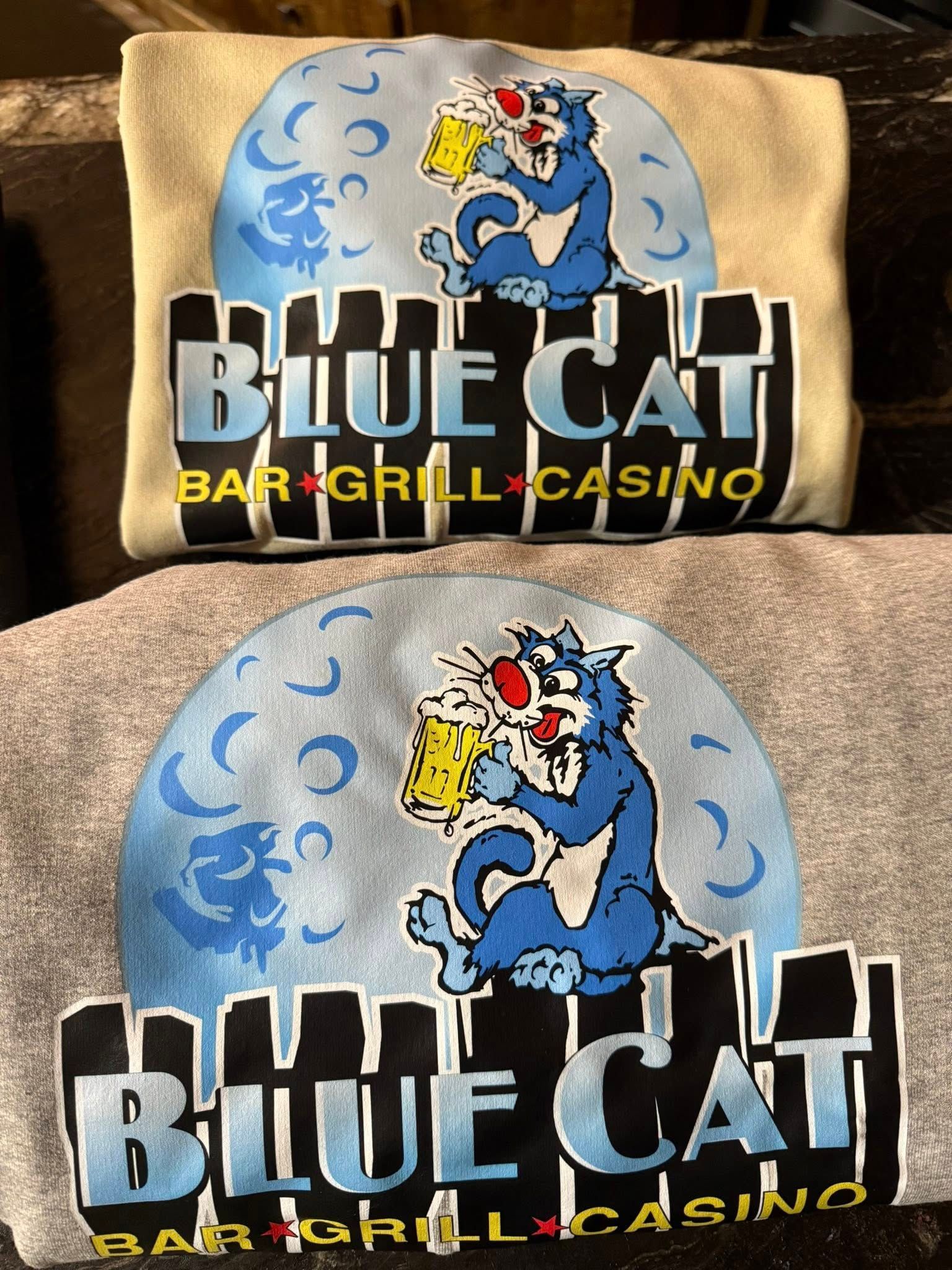 Blue Cat bar and grill casino logo on a beige shirt, featuring a blue cat in front of a full moon