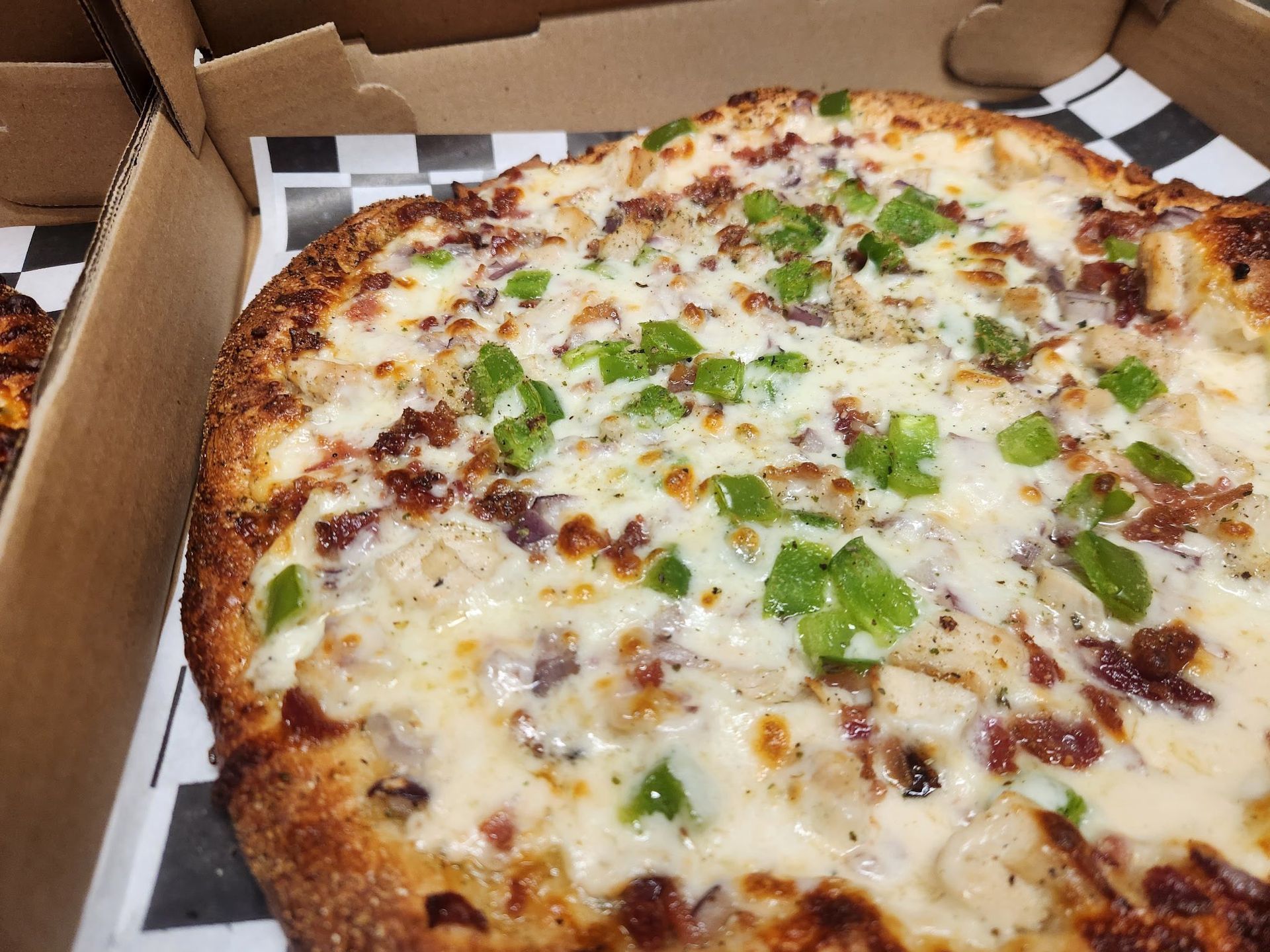 Cheesy pizza with green peppers and herbs in a cardboard takeout box