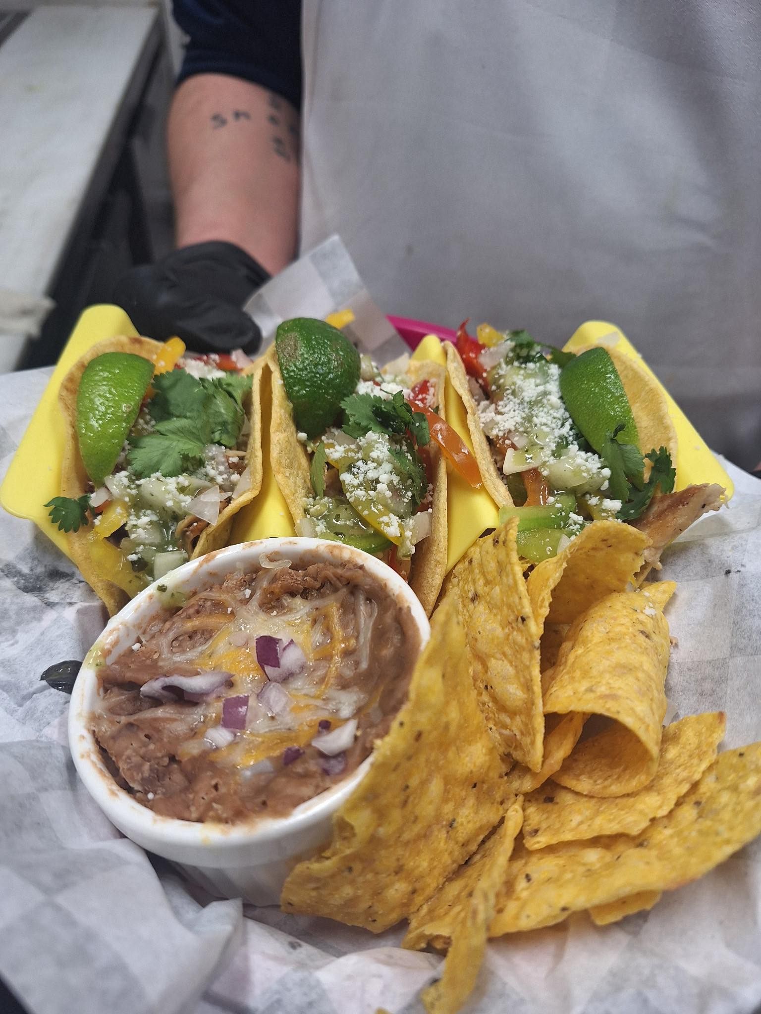 Three tacos with chips and a cup of refried beans on a tray