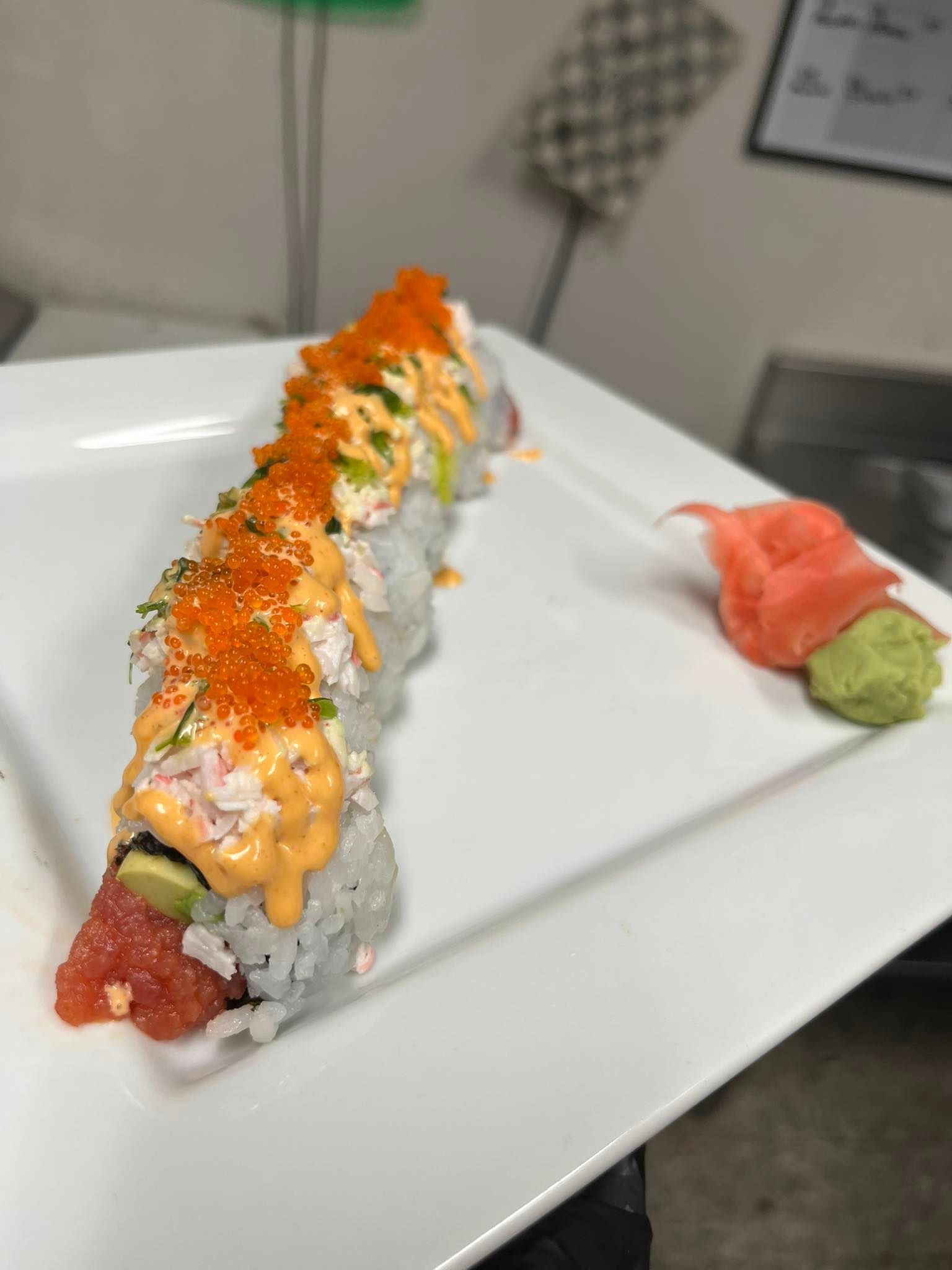 Sushi roll topped with orange sauce and fish roe on a white plate, with wasabi and ginger on the side