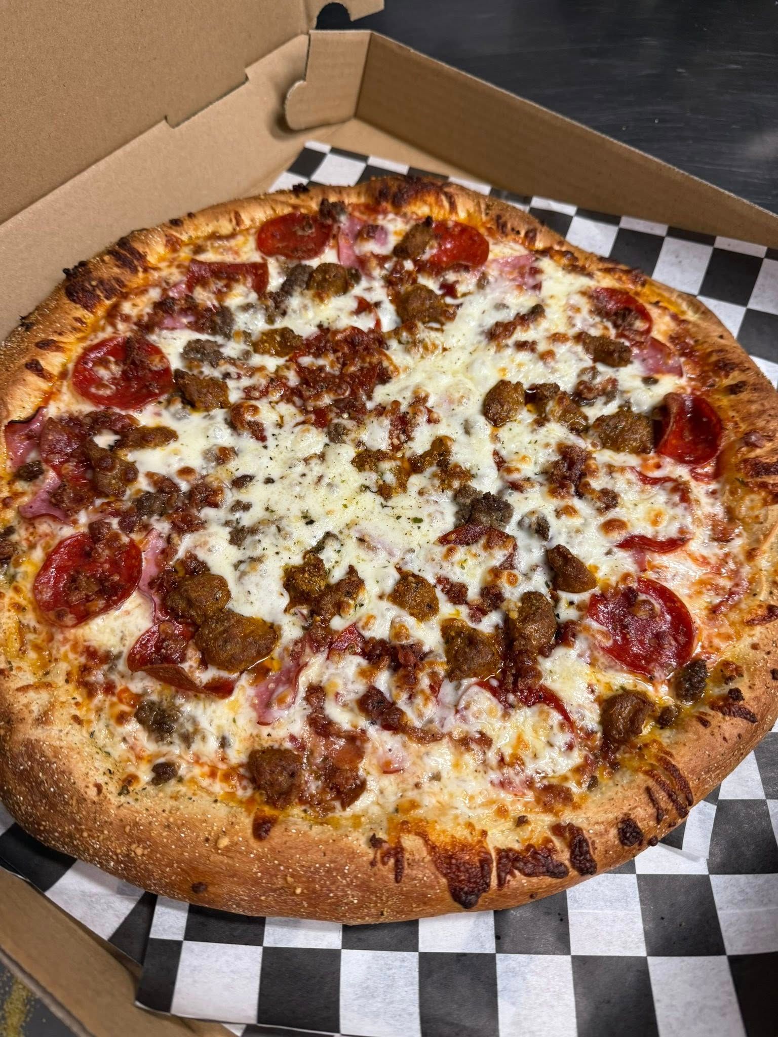 Pepperoni pizza in an open box on checkered paper, with a half-eaten slice missing