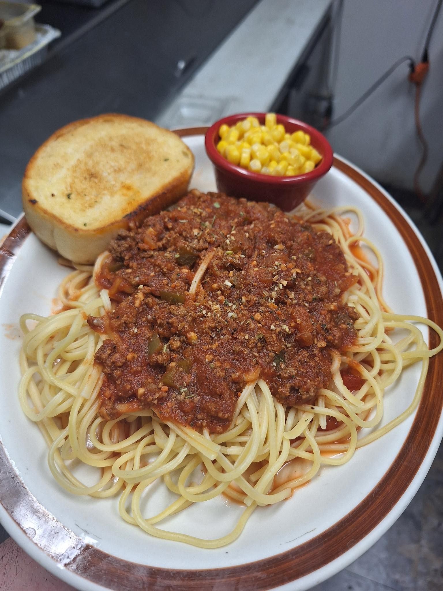 Plate of spaghetti with meat sauce, garlic bread, and corn on a red tablecloth