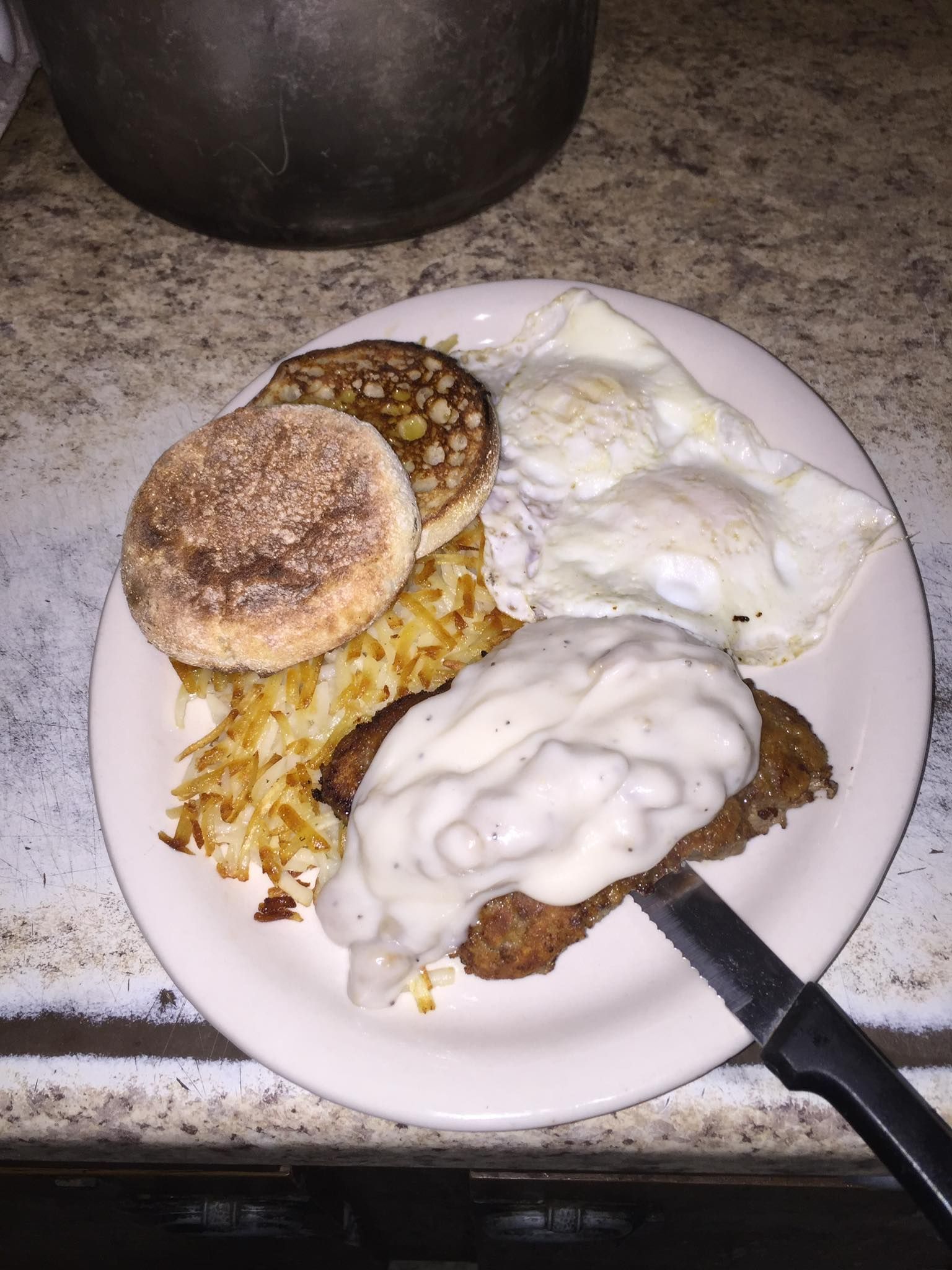 Plate of breakfast food with eggs, sausage, hash browns, and an English muffin with gravy