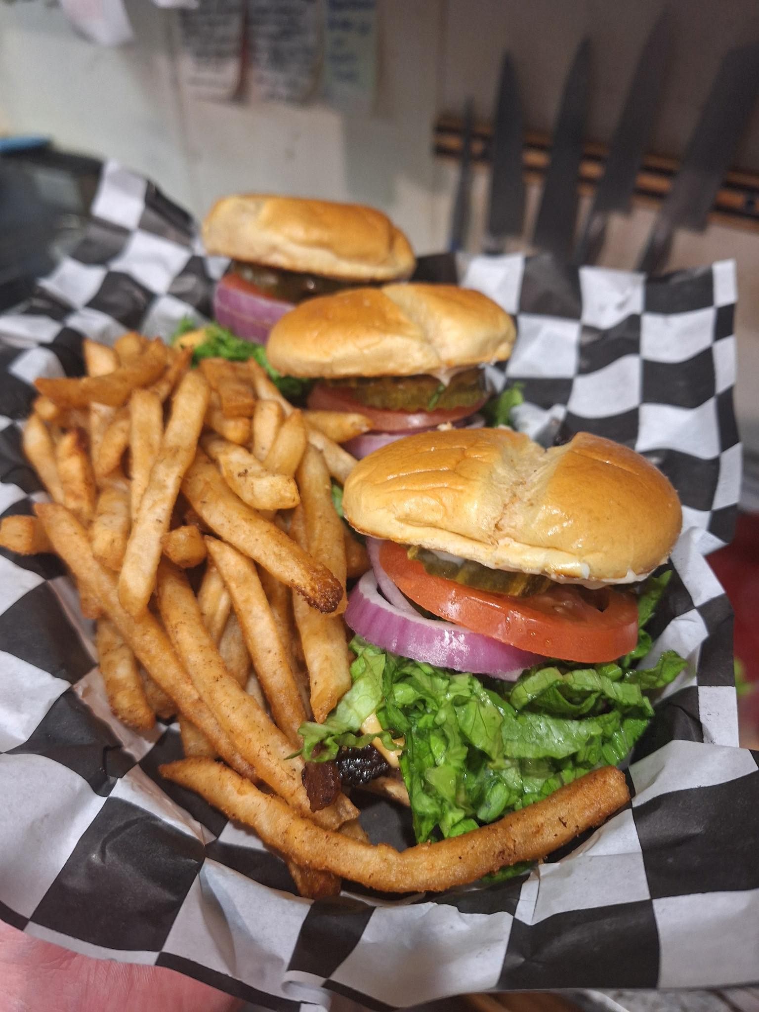 Three burgers and seasoned fries in a black-and-white checkered basket liner on a table.