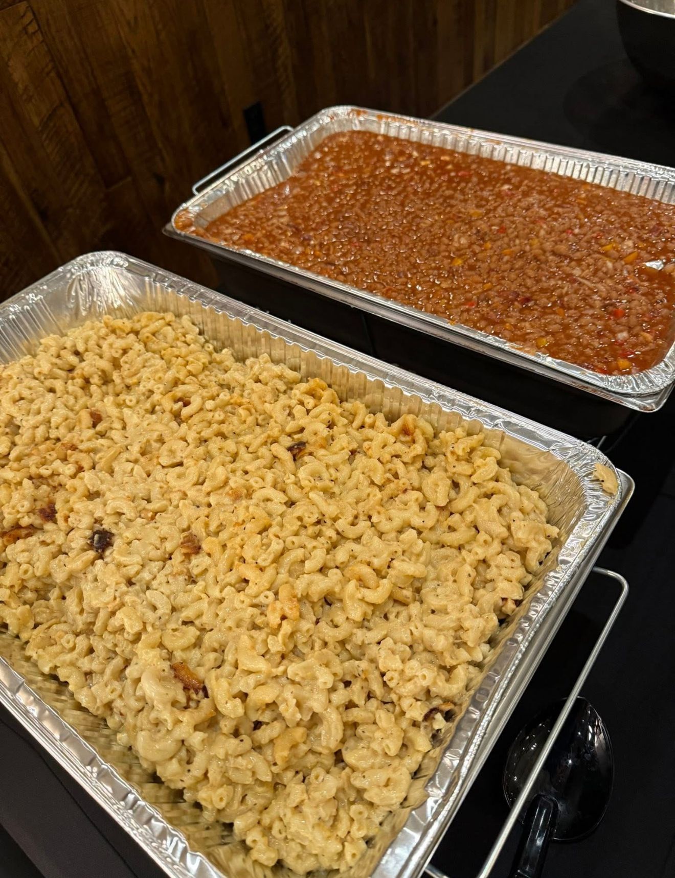 Two foil trays of baked pasta on a buffet table, one macaroni and one red sauce casserole