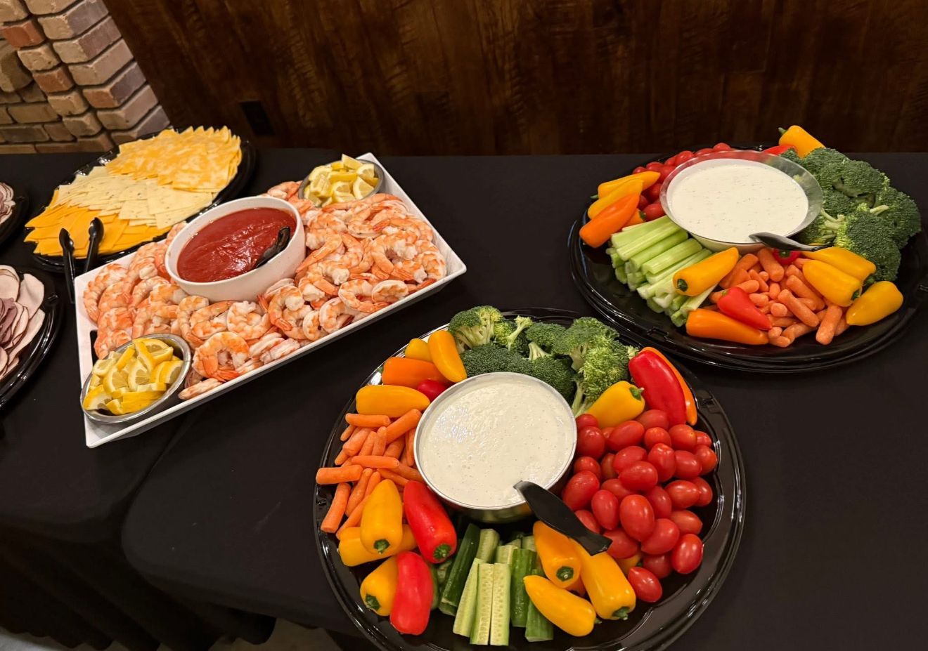Three colorful appetizer platters with vegetables, shrimp, crackers, and dip on a dark table