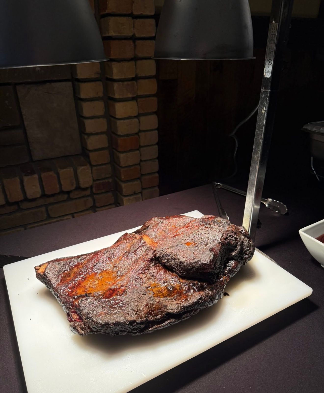 Grilled steak on a white plate with a knife, served on a dark table against a brick wall.
