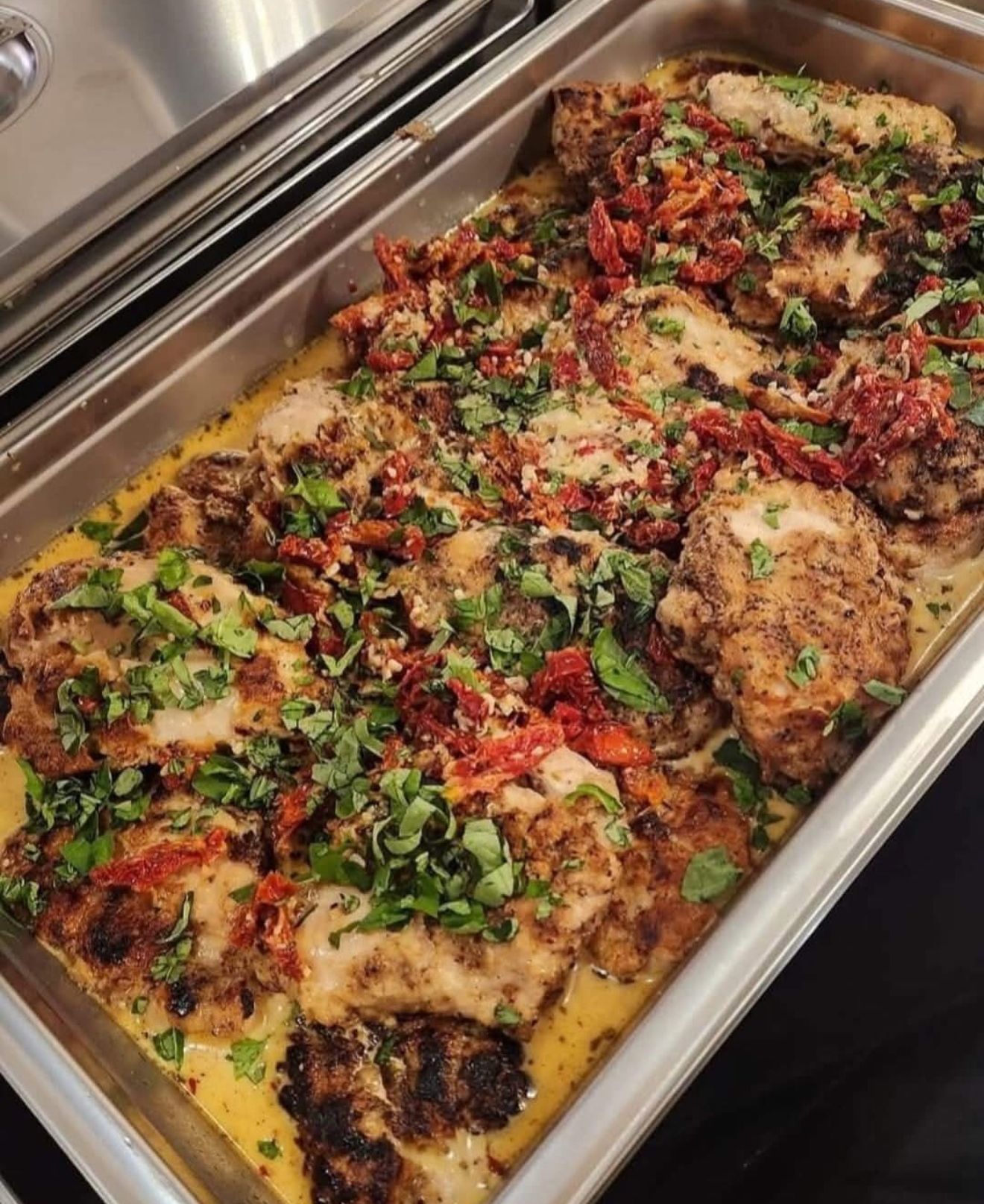 Tray of baked lasagna topped with herbs, red sauce, and melted cheese in a stainless-steel pan